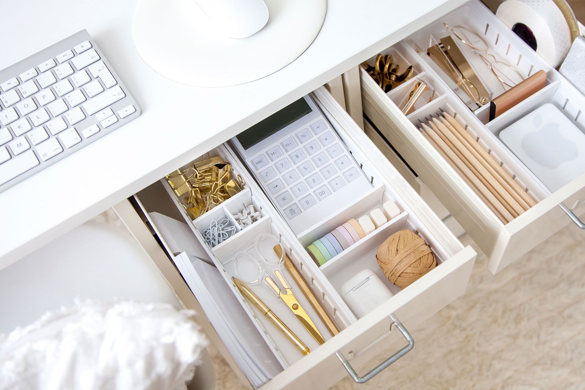 An open drawer in a desk, containing organized compartments full of office supplies and a calculator.
