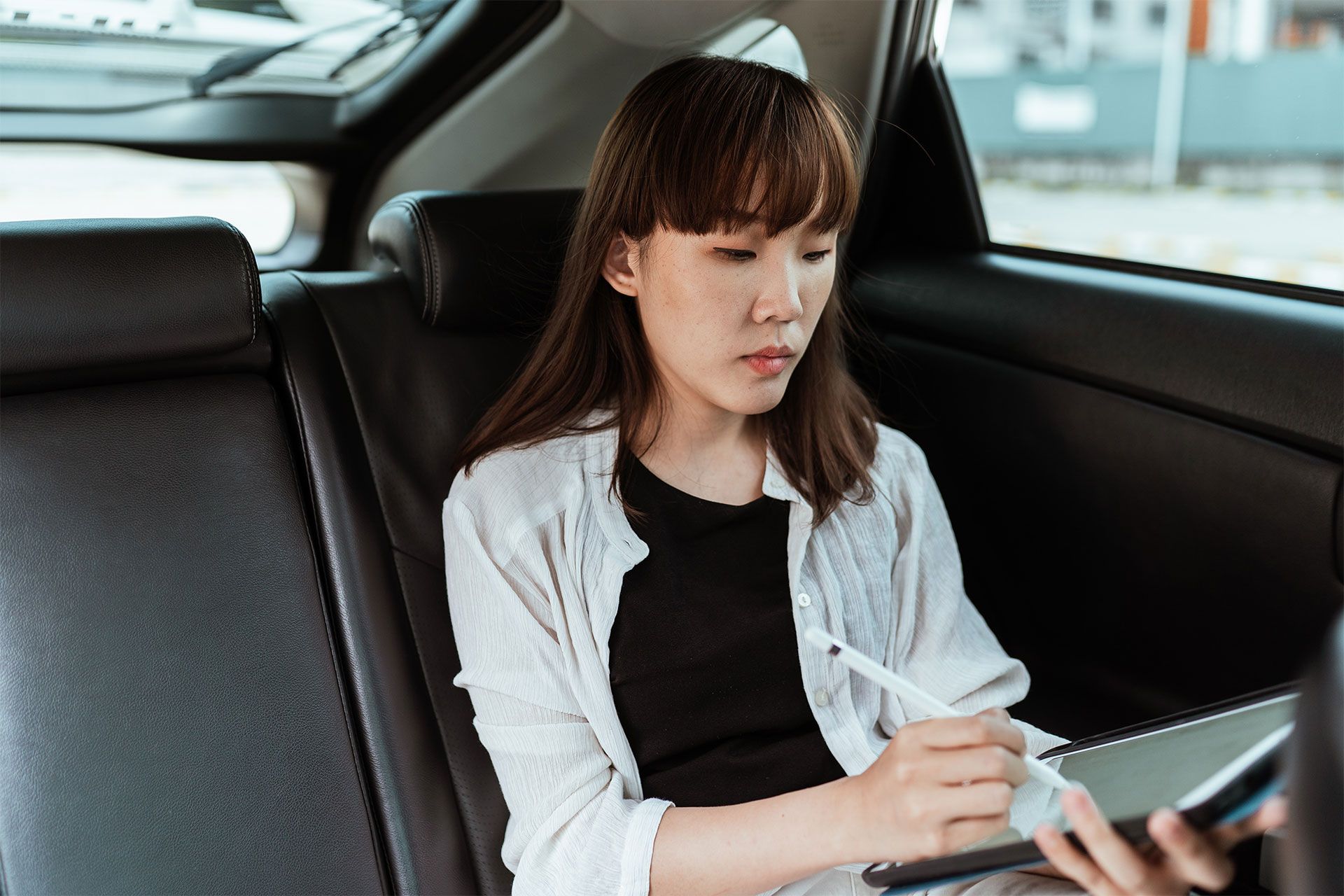 A person sat in the back of a car, signing a PDF document on a tablet.