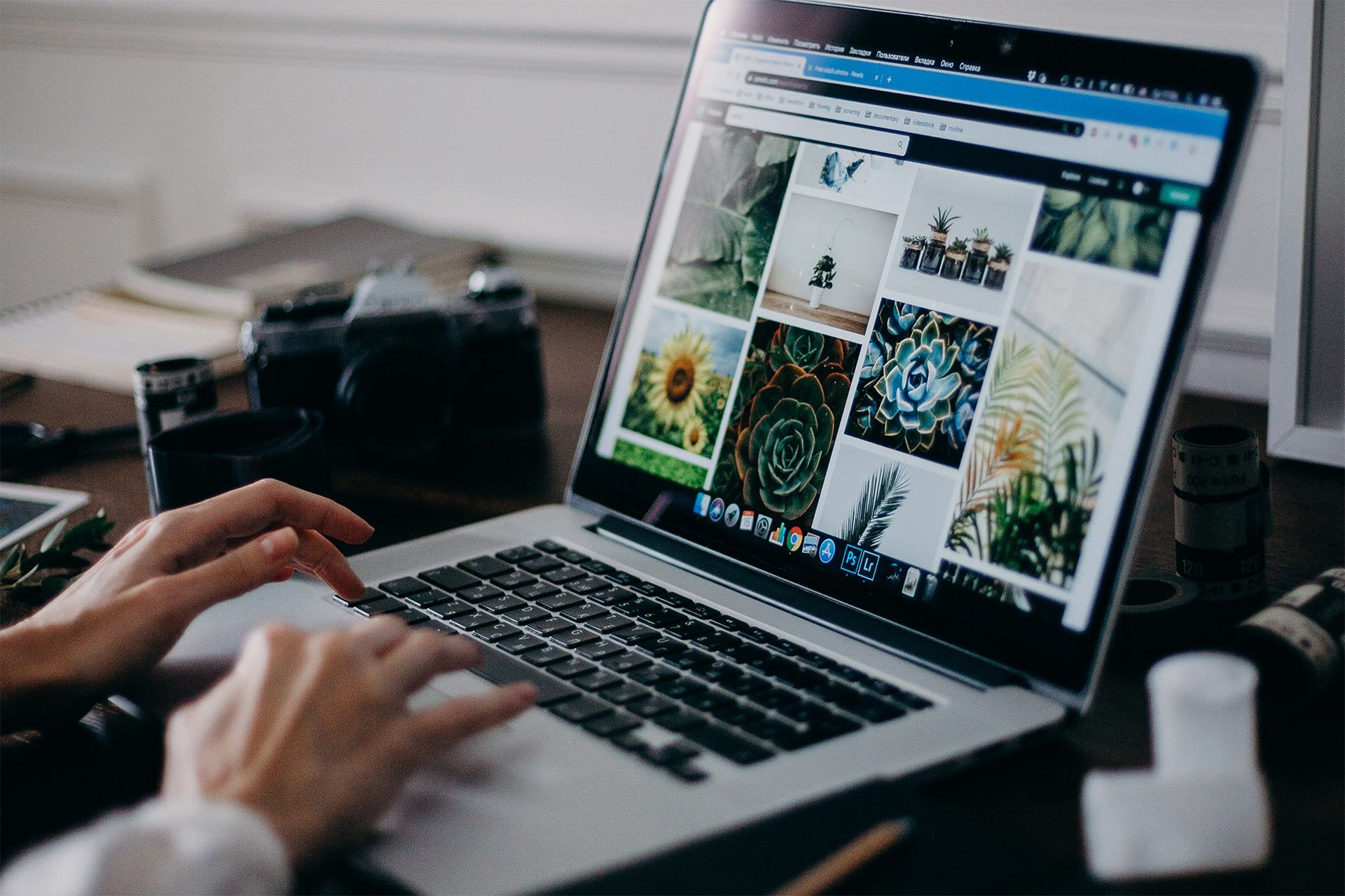 A person uses their laptop to browse and organize their photos, a camera on the desk beside them.