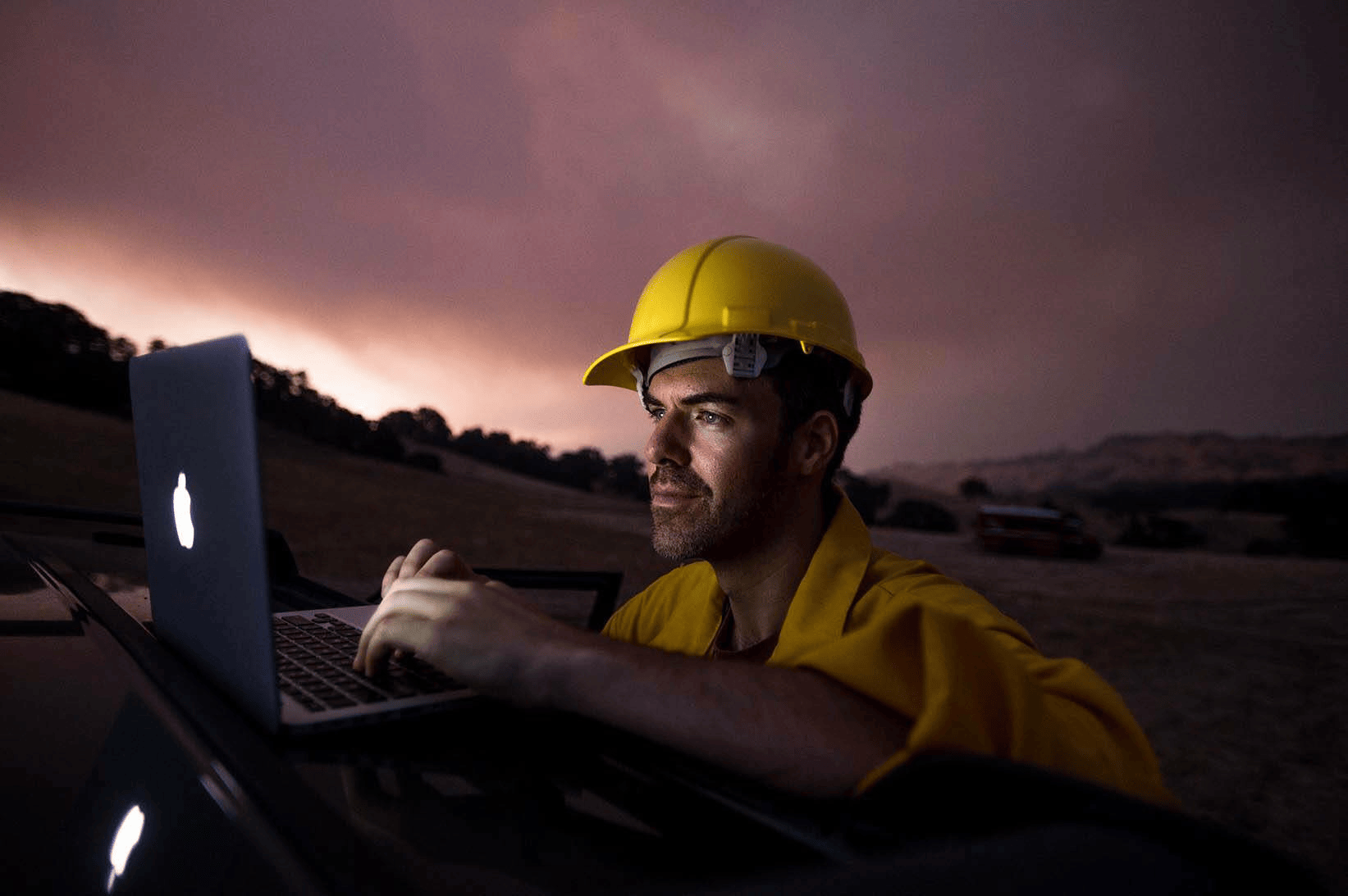 Photographer Josh Edelson works on his laptop computer while a dark, smoky landscape is seen in the background.