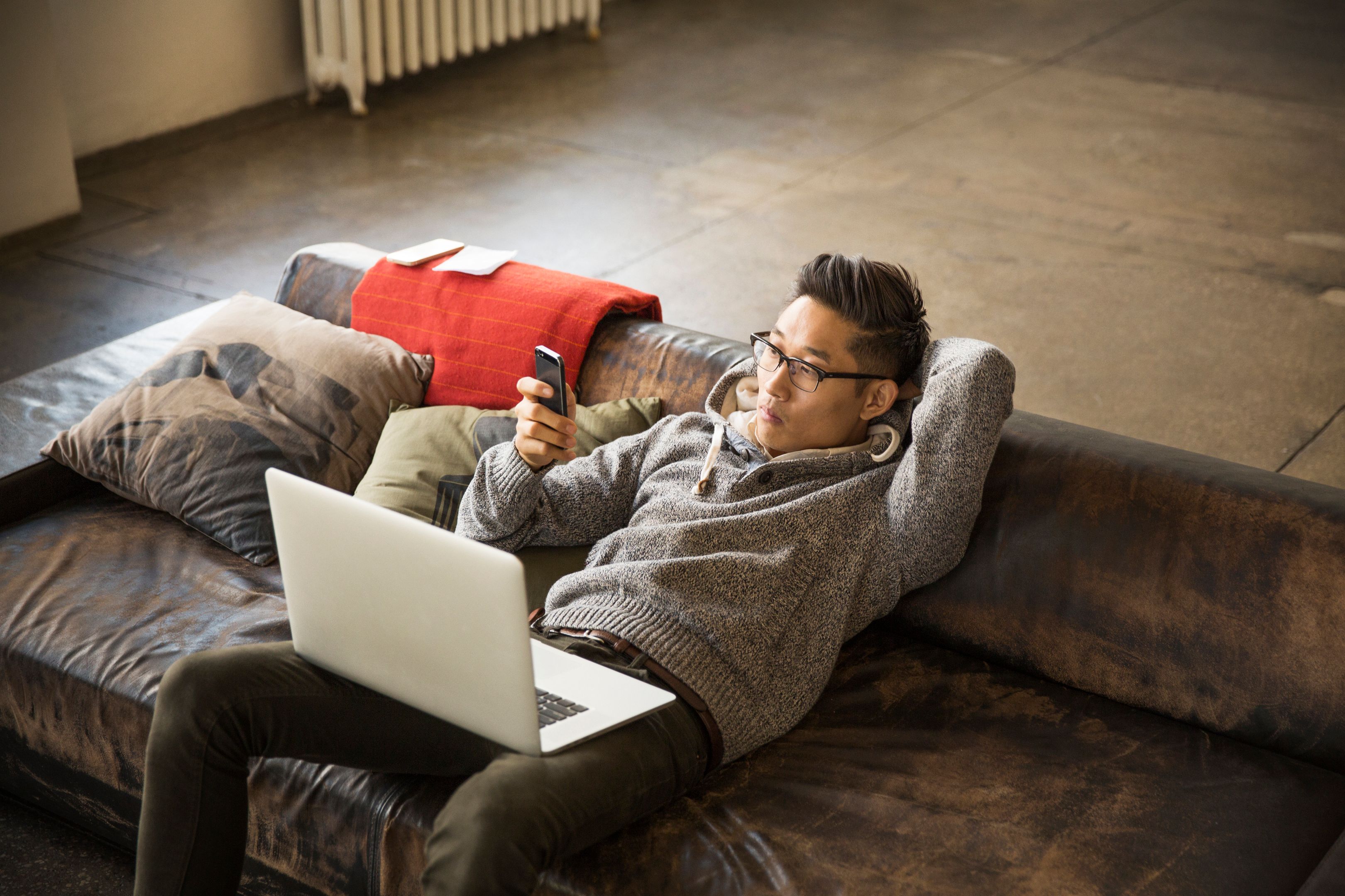 Man looking at phone with a laptop on his lap.