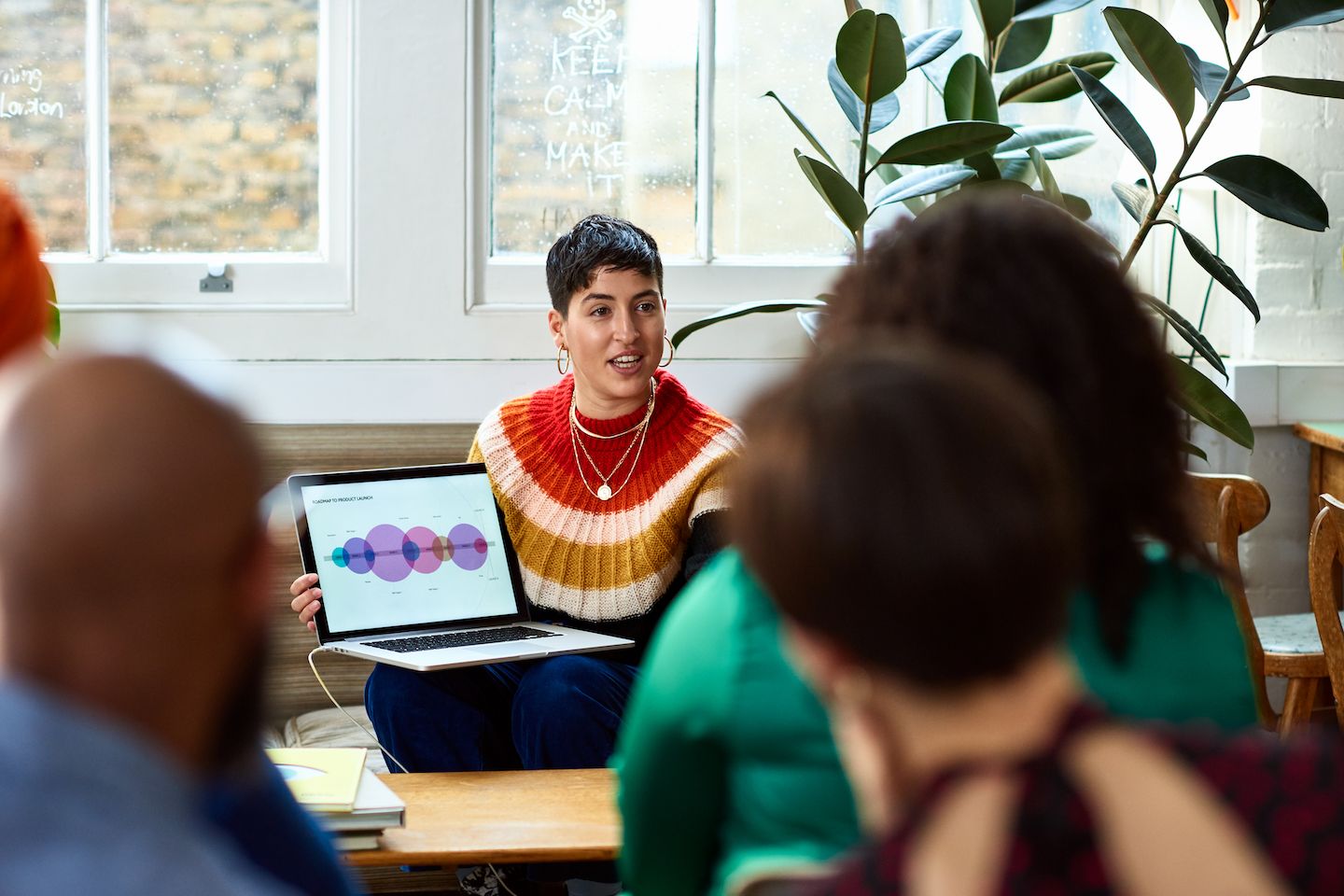 A person shows her laptop screen, full of data analysis graphs, to a team of creative business people.