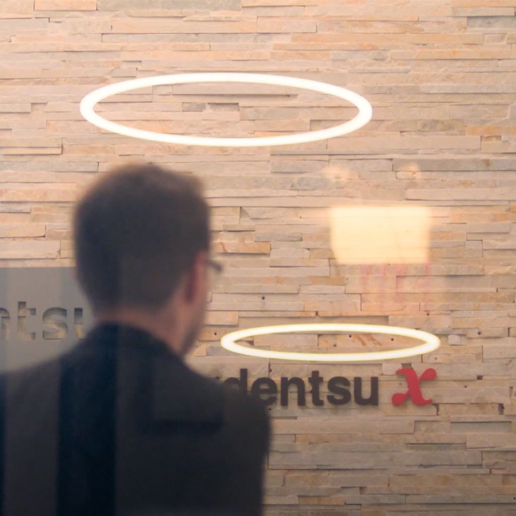 Un hombre frente al logo de Dentsu colocado en una pared de ladrillo 