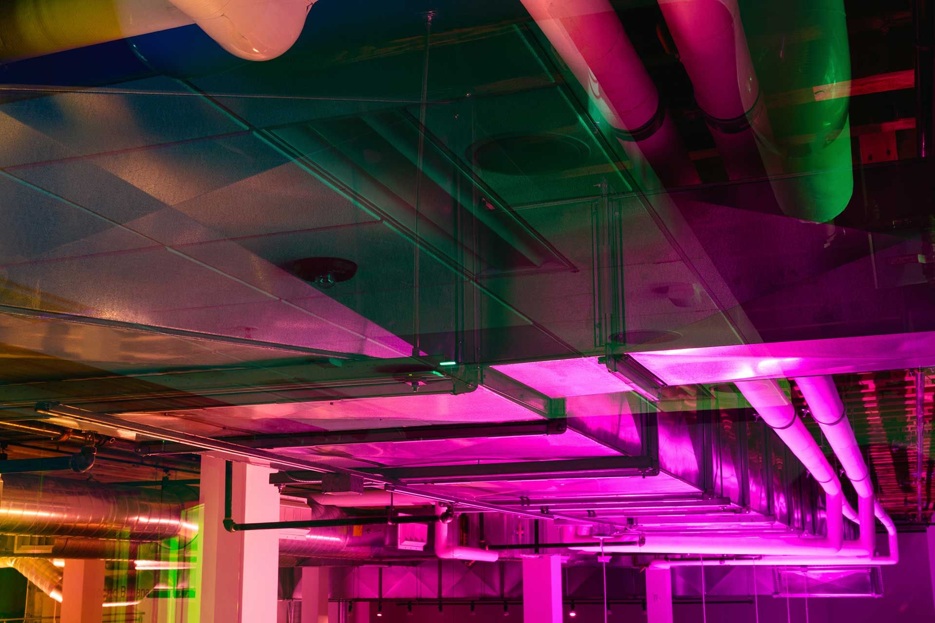 Pink light cast onto the ceiling showing air-conditioning ducts