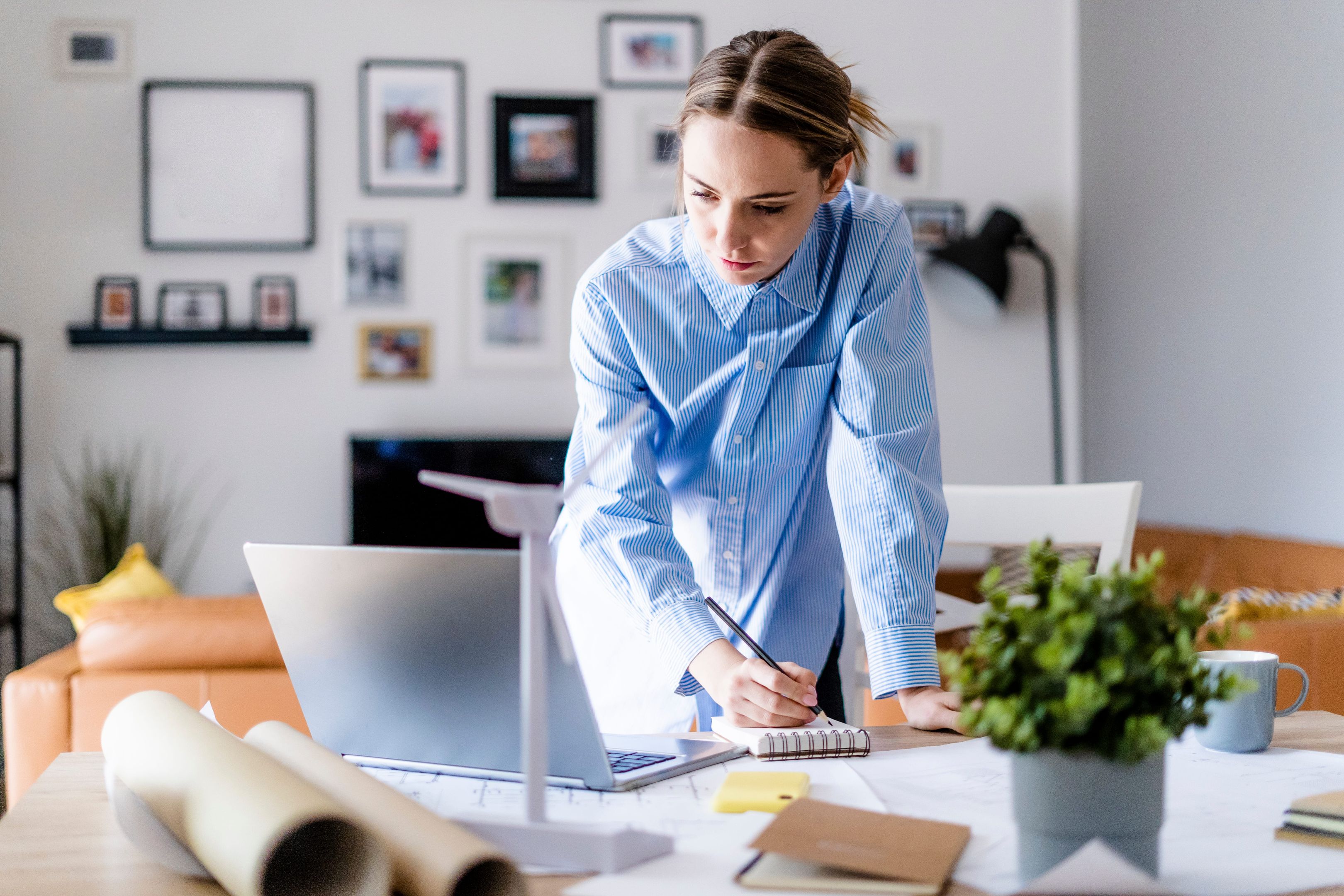 A person writes a list for a writing services invoice while glancing at a file on their laptop.
