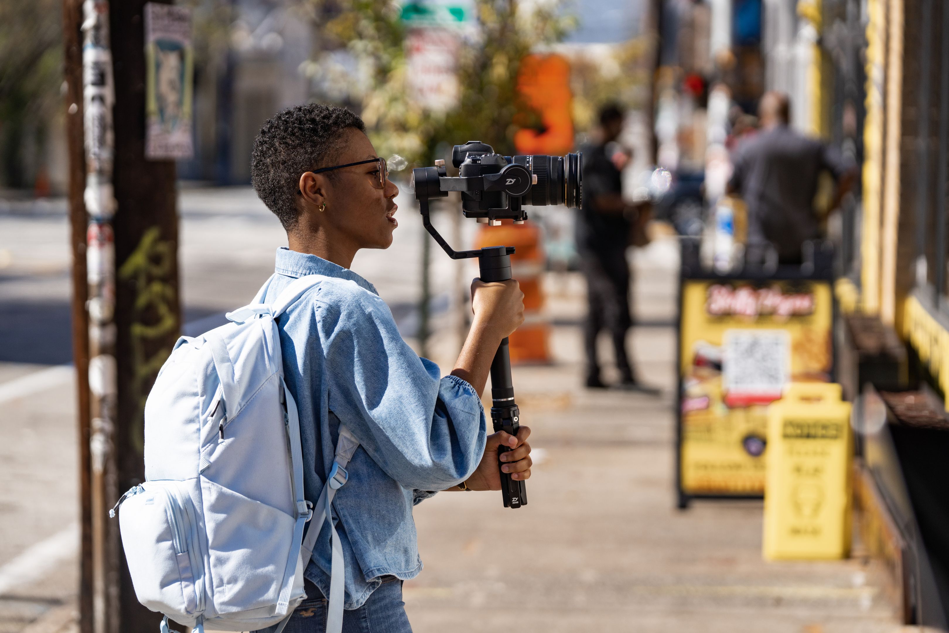 A videographer holds a professional camera mounted on a stabilizer as they capture raw footage to send to a video editor.
