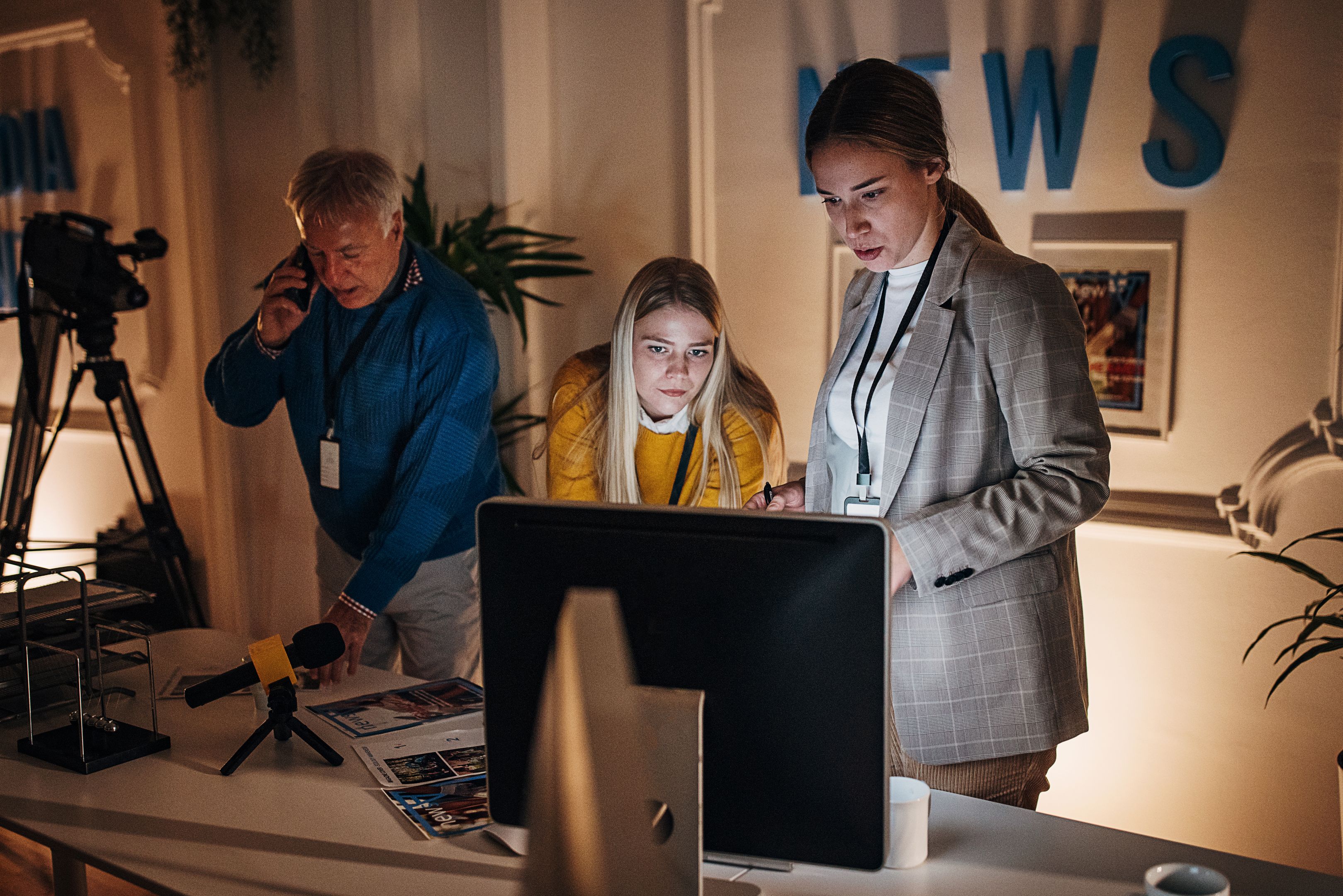Tres personas trabajando en una oficina moderna, una persona al teléfono y otras dos mirando una pantalla de computadora.