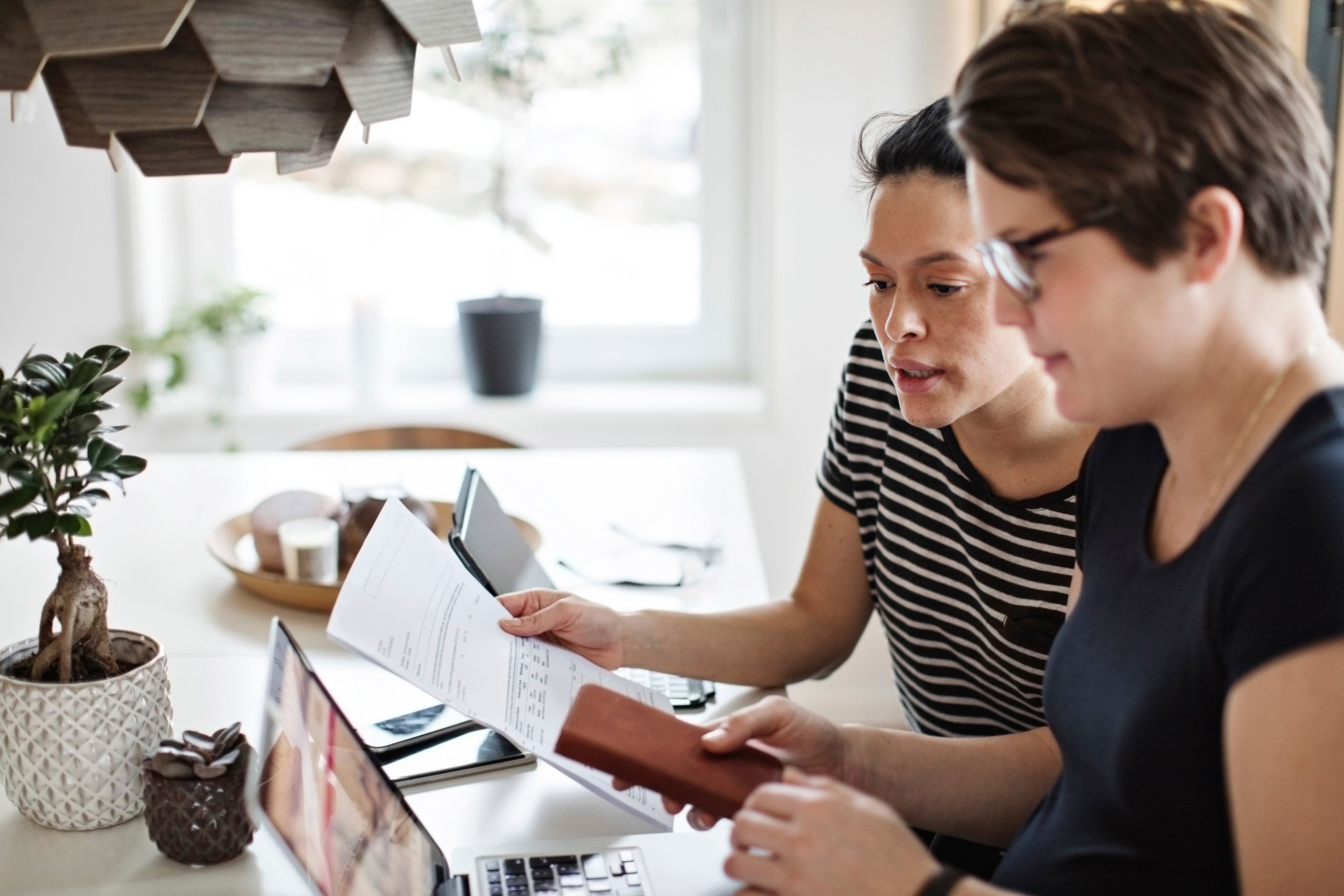 Two people sat at their kitchen table look at their laptops and an invoice while reviewing their household budget.