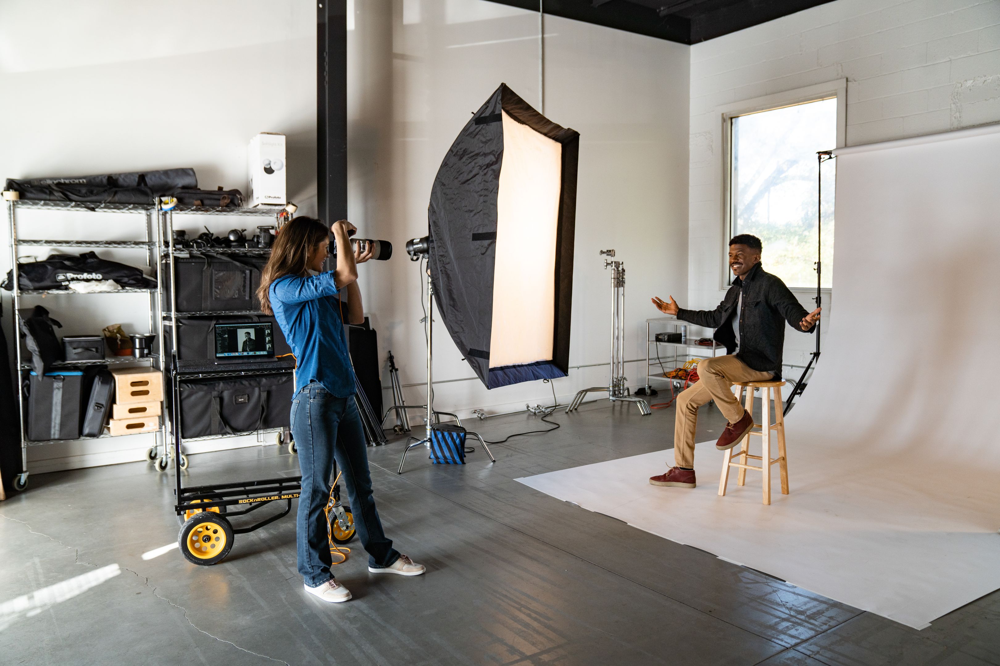 Fotógrafo apuntando la cámara a una persona sentada en el taburete de un estudio