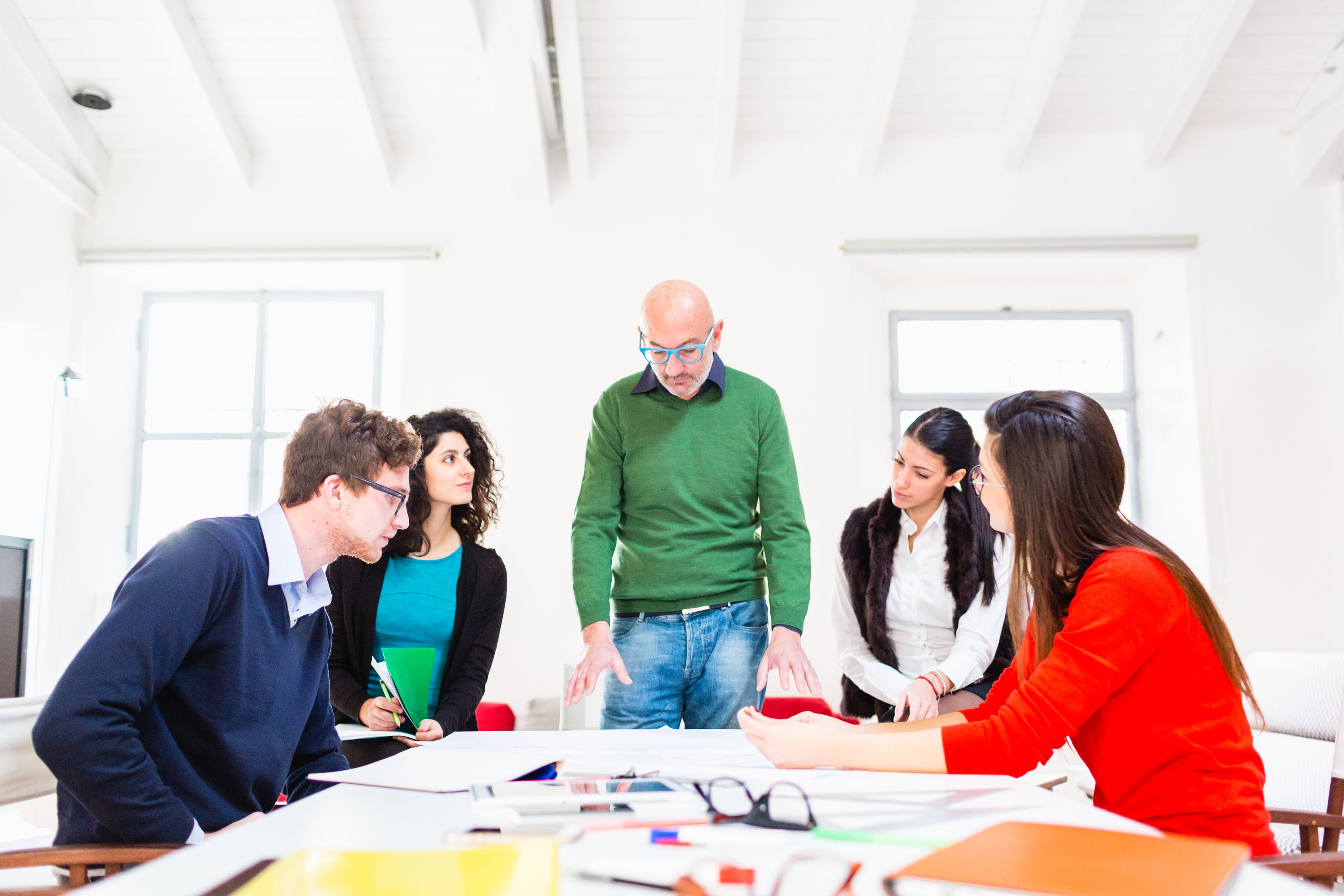 A team of people sit and stand around a desk, discussing how to set up a DMAIC process to support their project.