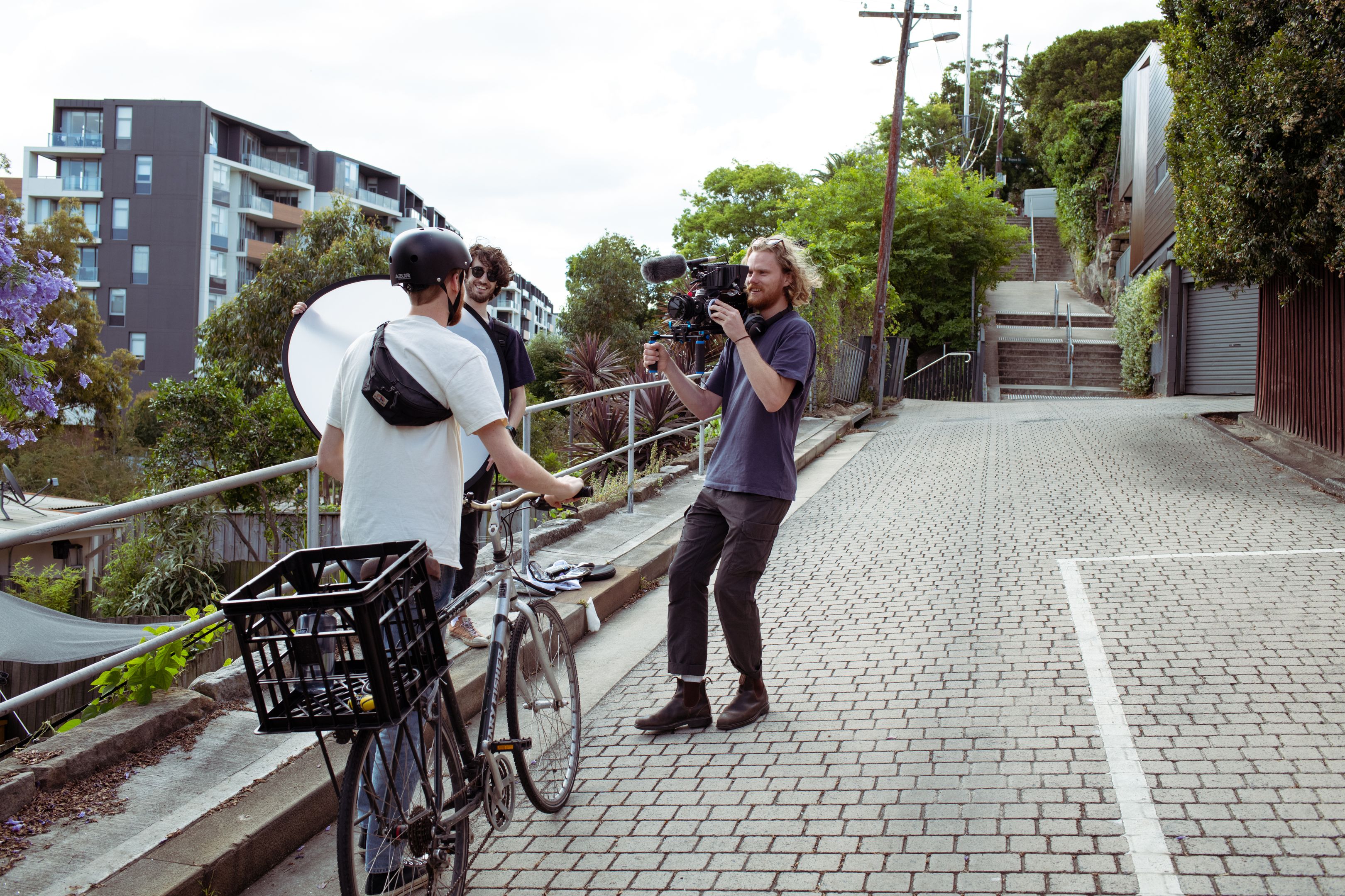 Person auf einem Fahrrad, der mit Filmemacher mit Kamera spricht, während eine weitere Person einen Reflektor hält.