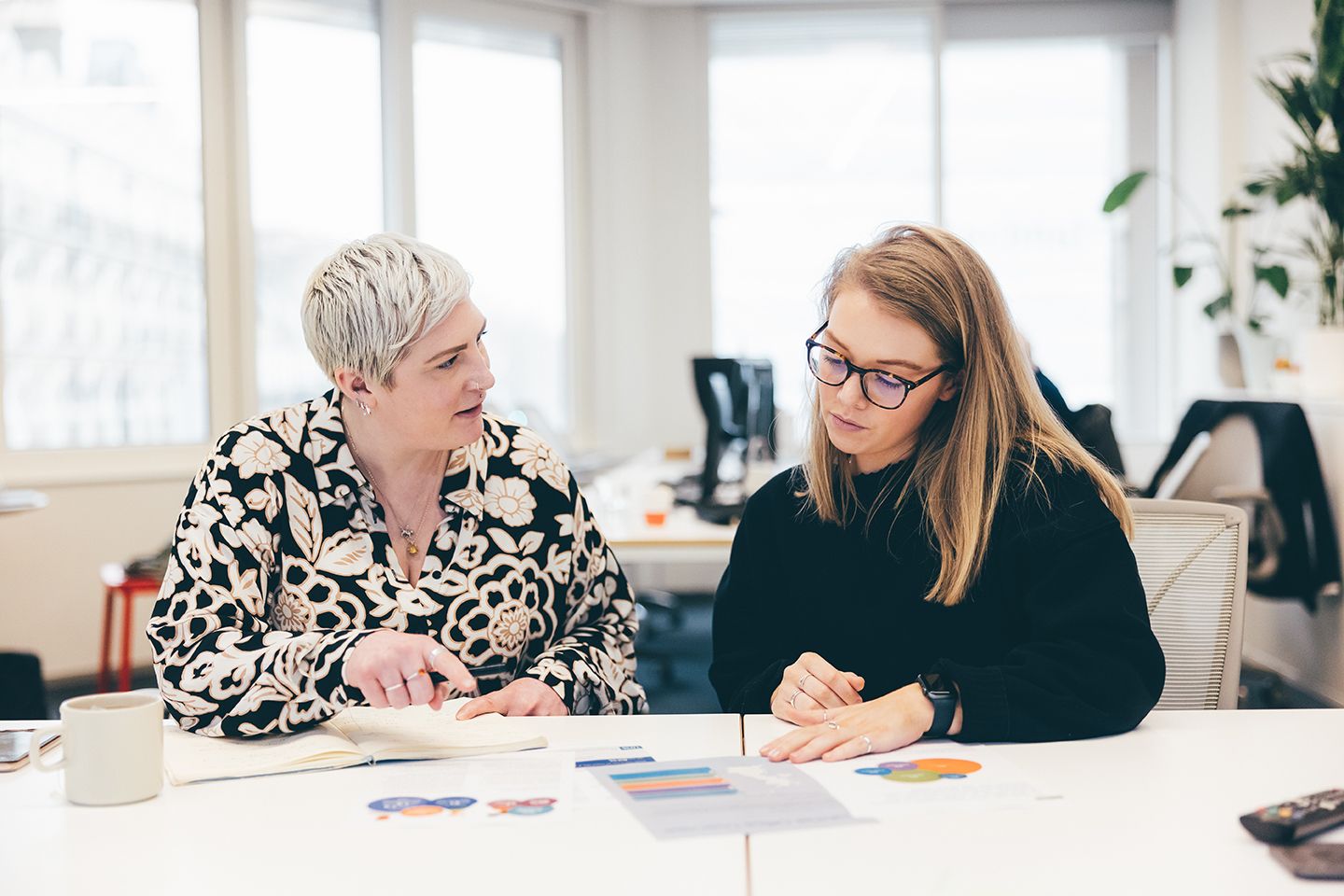 Two women sit at a conference table and look at printed charts.