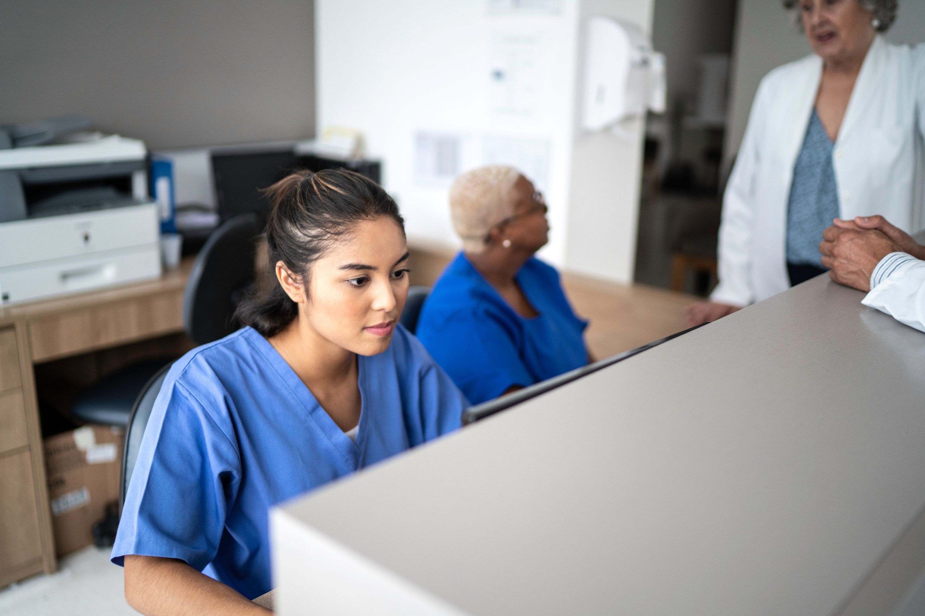A healthcare professional accesses data on their computer in a busy hospital setting.