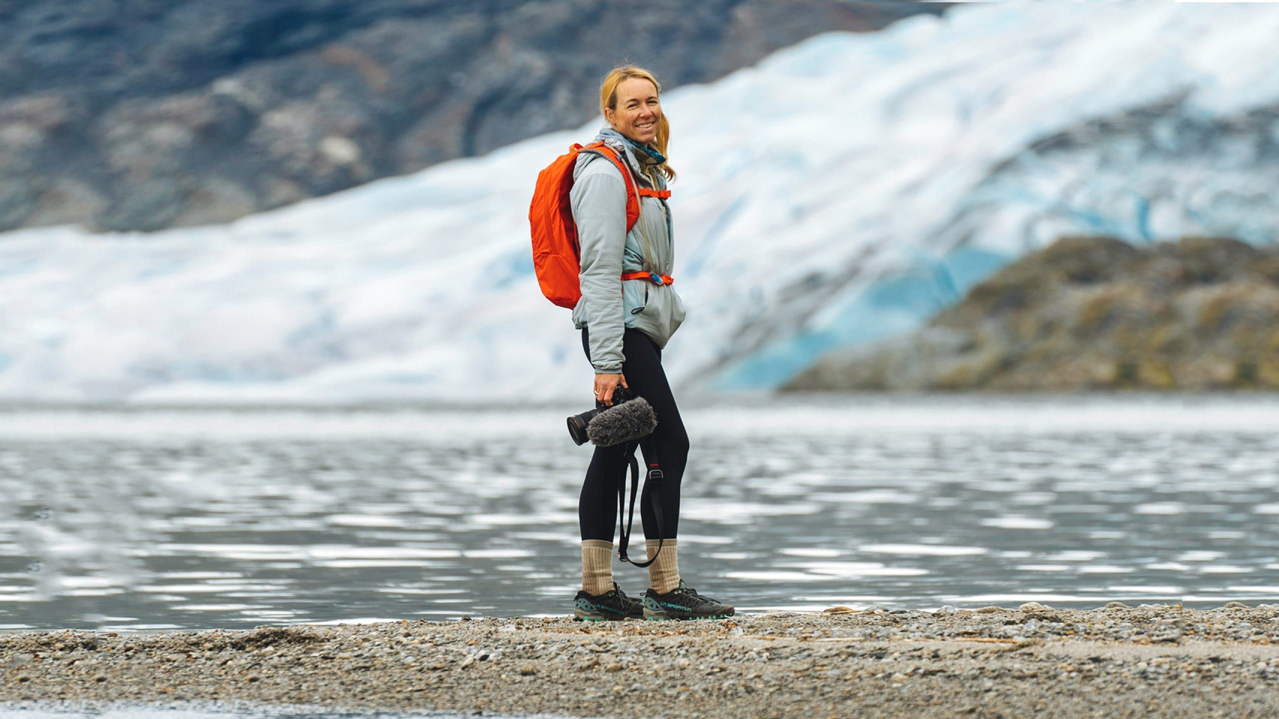 A woman stands in front of a lake holding a camera.