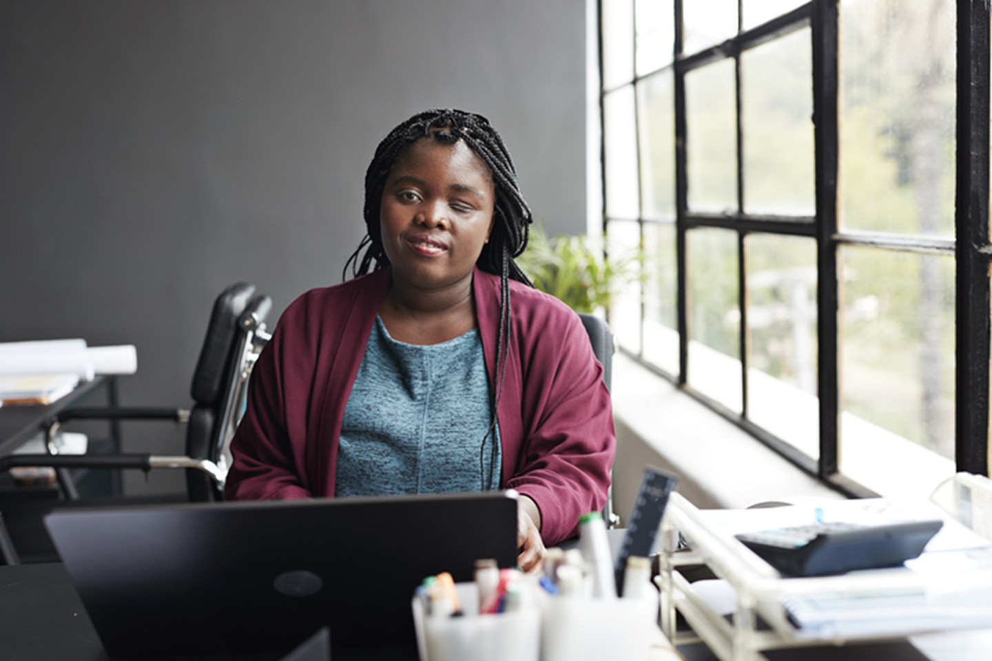 Femme assise à un bureau avec un ordinateur portable, regardant vers la caméra dans un bureau moderne.