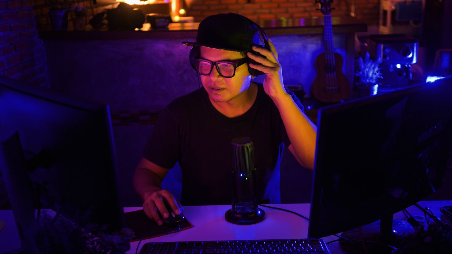 A man with headphones on sitting in front of 2 computer screens