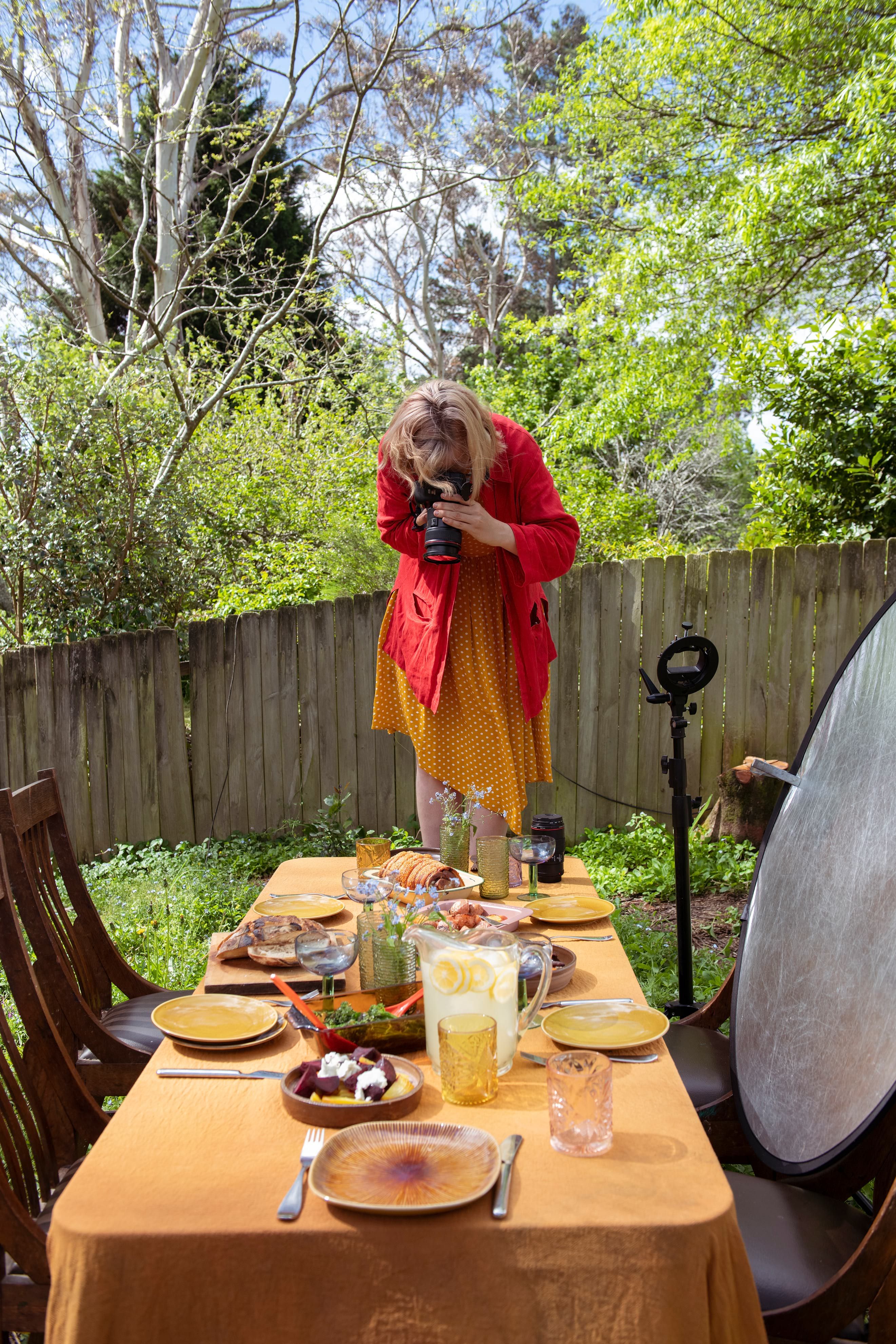 A woman takes a photograph of a table with food on it.