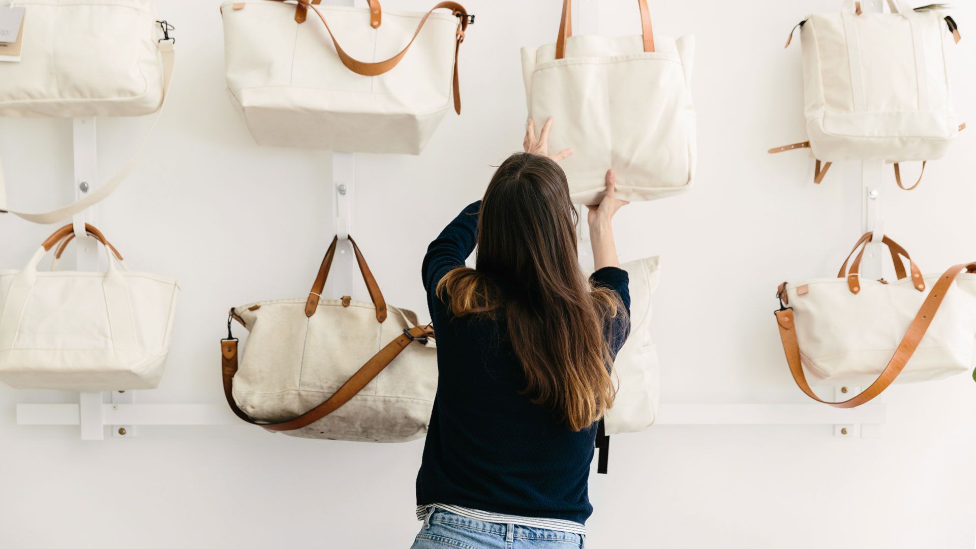 A person hanging white tote bags on a white wall