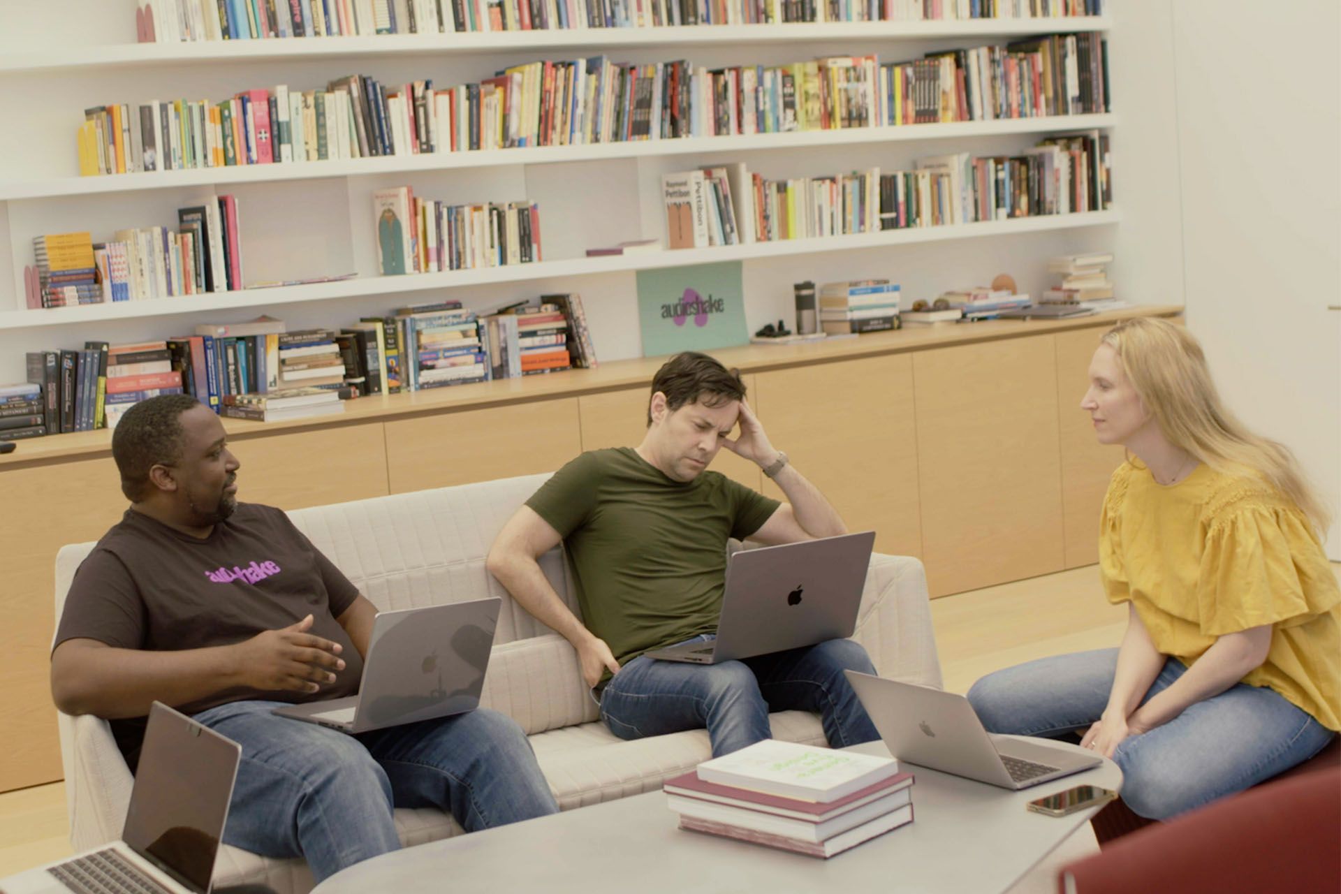 Trois personnes discutent sur un canapé placé devant une bibliothèque