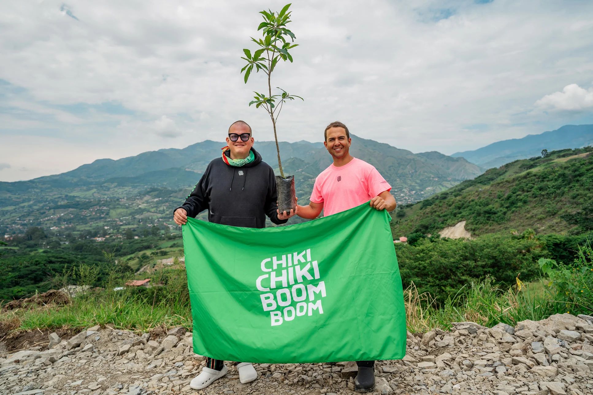 I fondatori di Chiki Chiki Boom Boom con in mano un cartello e un piccolo albero in cima a una montagna