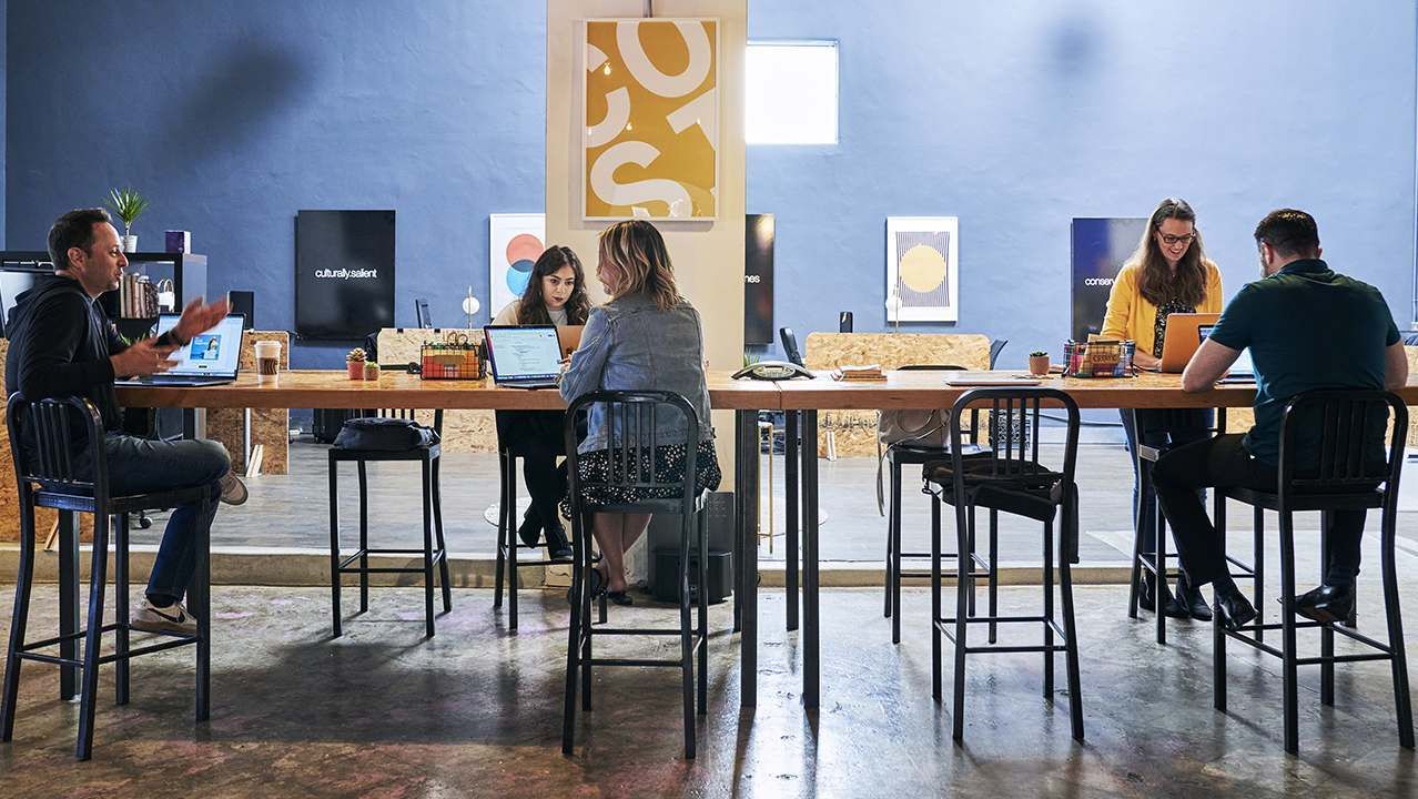 Five individuals work and talk at a communal table