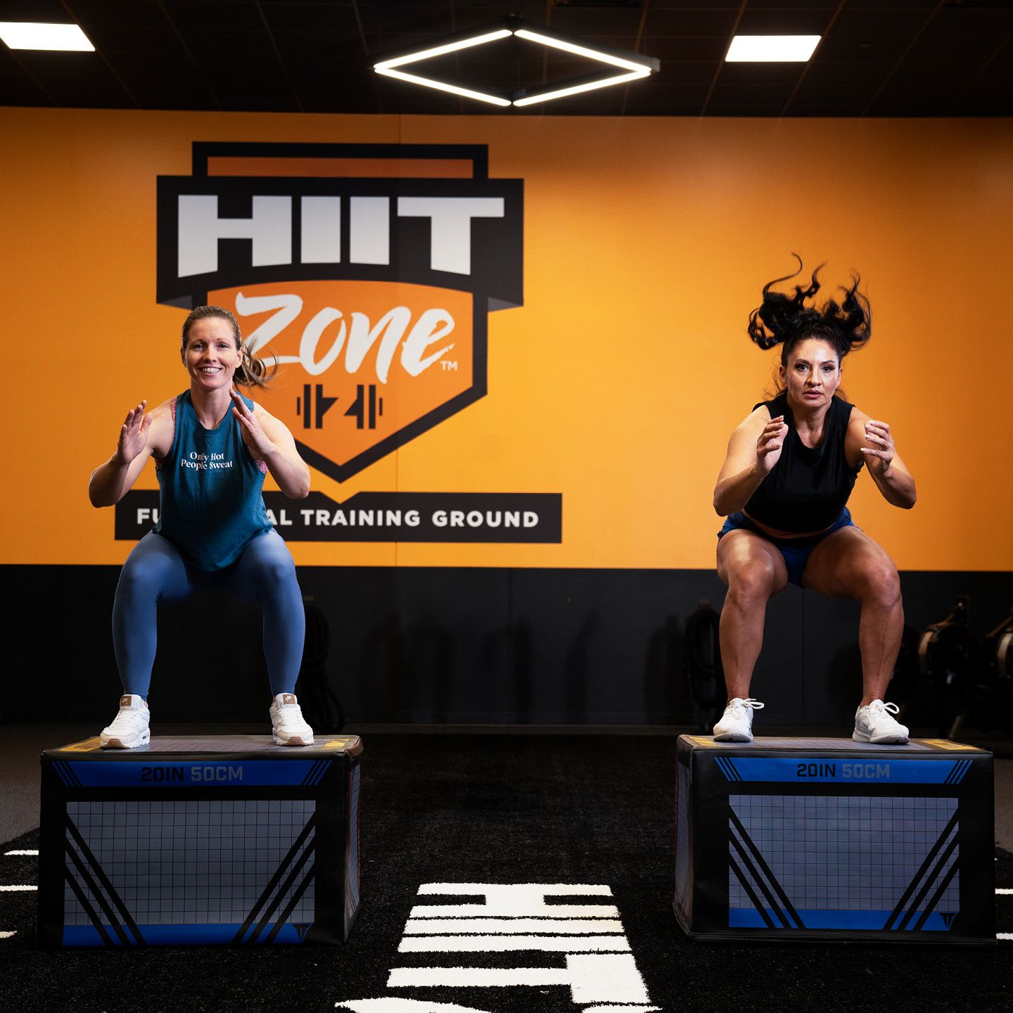 Two women landing on a jump box within the HIIT Zone of a Crunch Fitness.