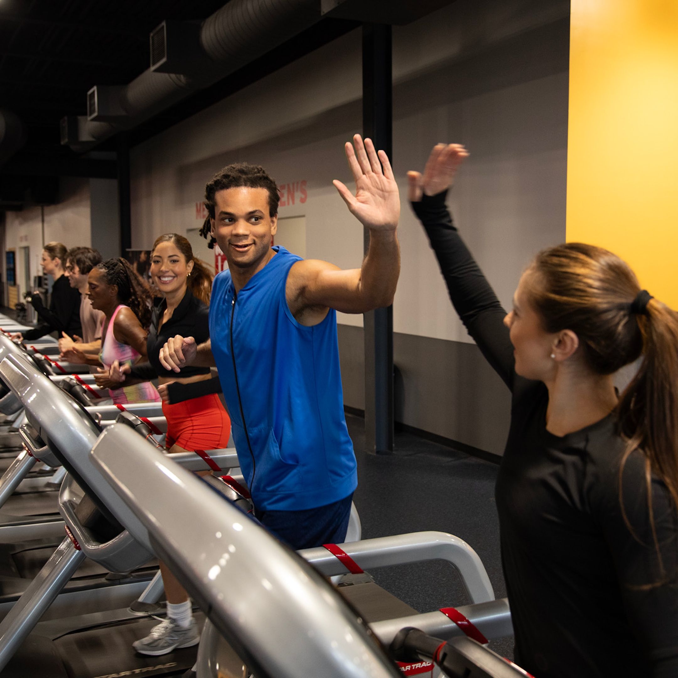 Row of people running on treadmills with two people high fiving in the middle.