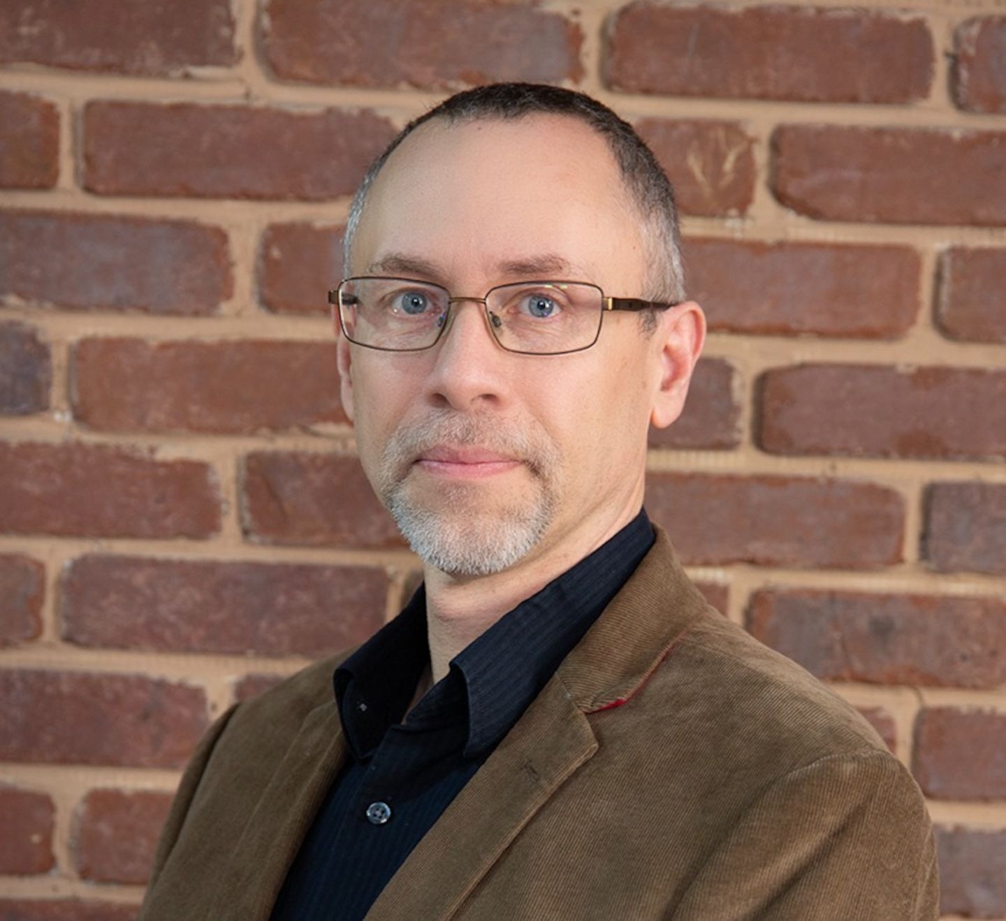 William Schellhaas in a brown sport coat standing in front of a brick wall.