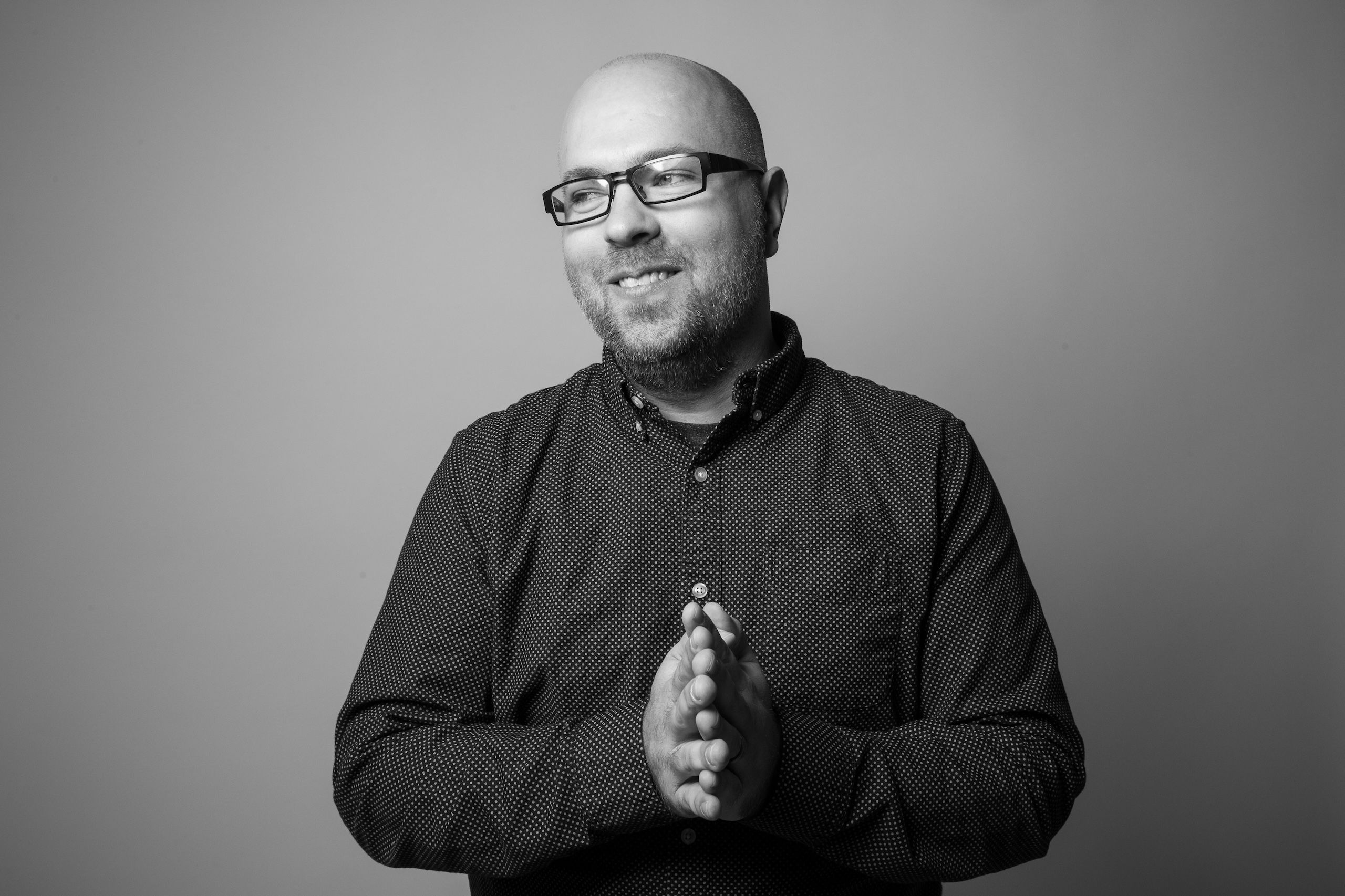 Adam Nielson w czarnej koszuli z guzikami i okularach stojący do czarno-białego zdjęcia