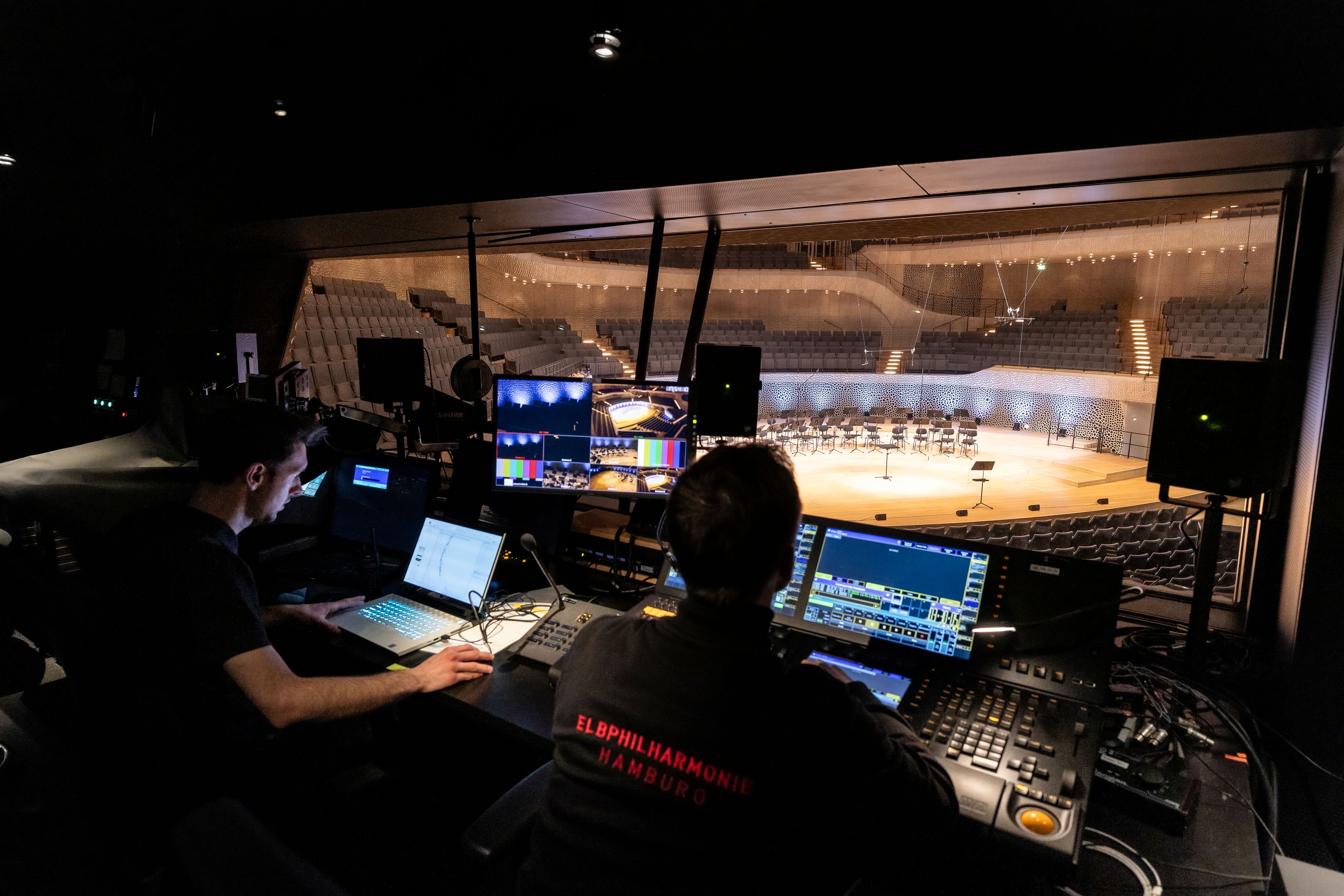 Two people working on a sound system overlooking an orchestra stage