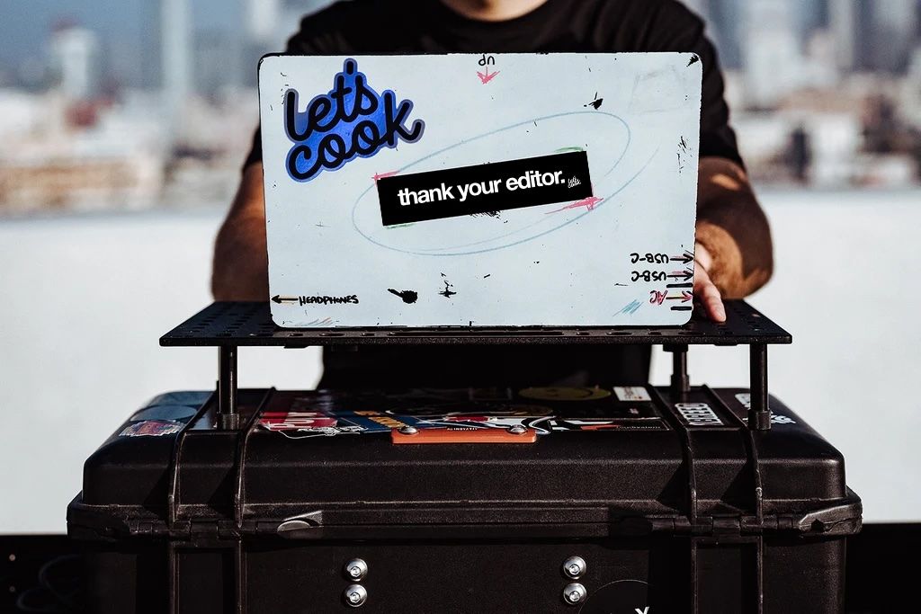 Laptop sitting on a cart with filming equipment outside and stickers that say let’s cook and thank your editor.