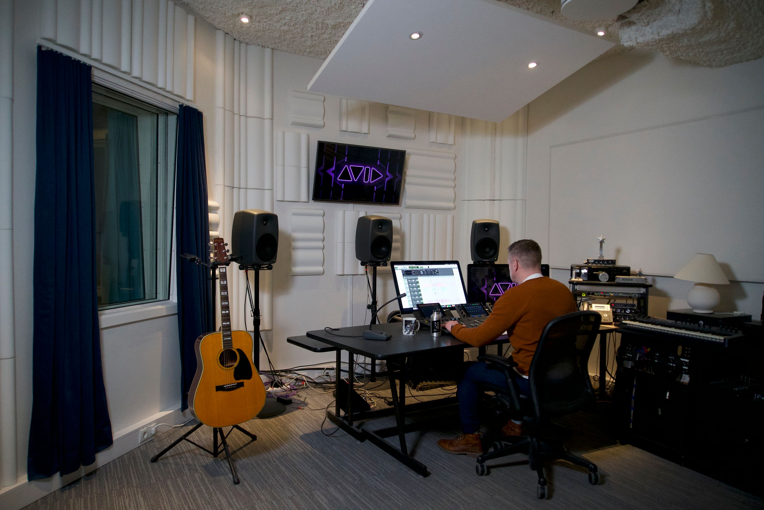 Man working at an editing suite next to a guitar in a sound-proof room.