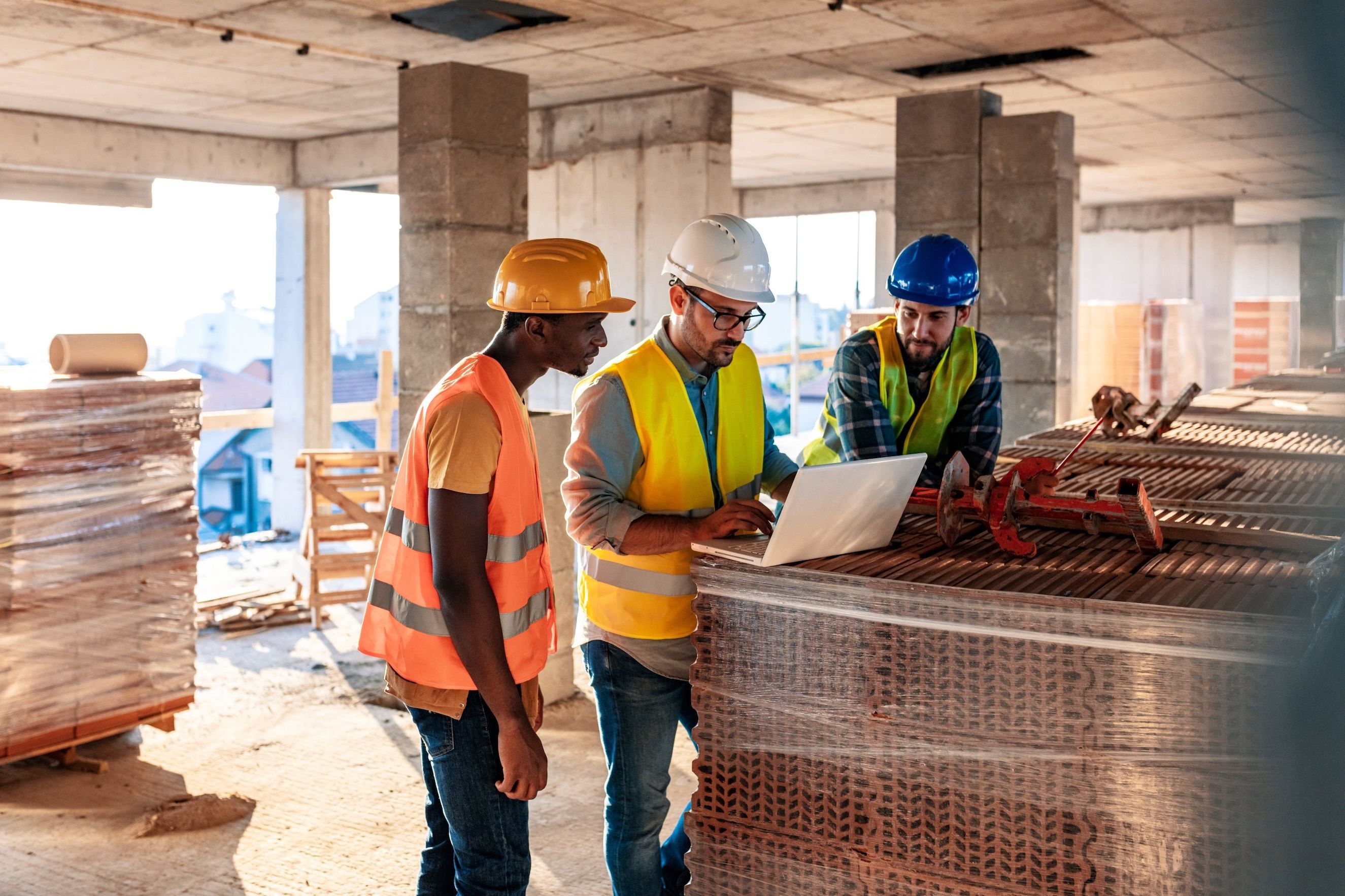 Three men in hard hats on a construction site looking at a computer
