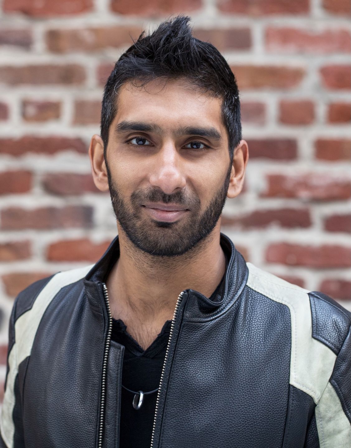 Rahul Vohra standing in front of a brick wall wearing a black and white leather jacket.