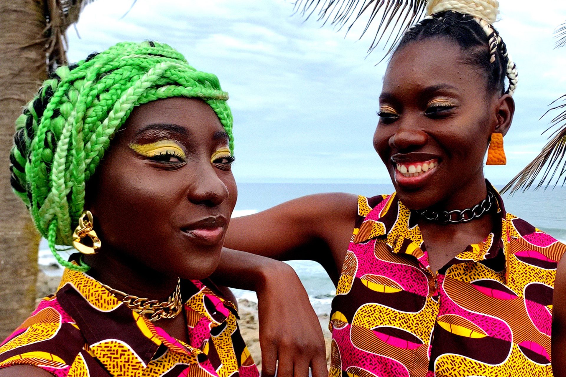 Two women in brightly coloured clothes in front of a palm tree
