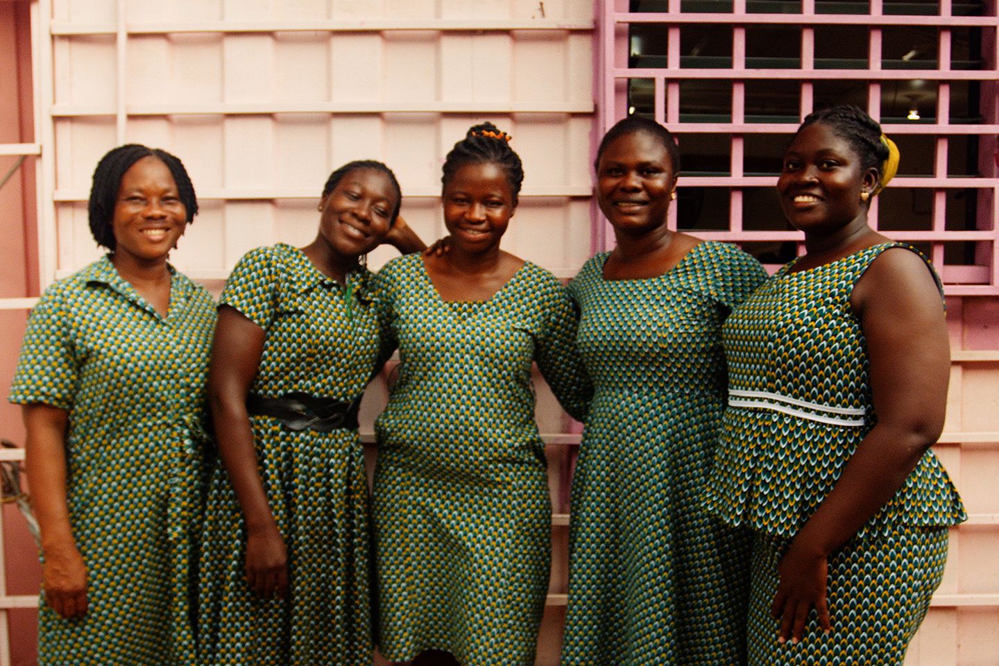 Пять женщин в зеленых платьях стоят перед розовым зданием.