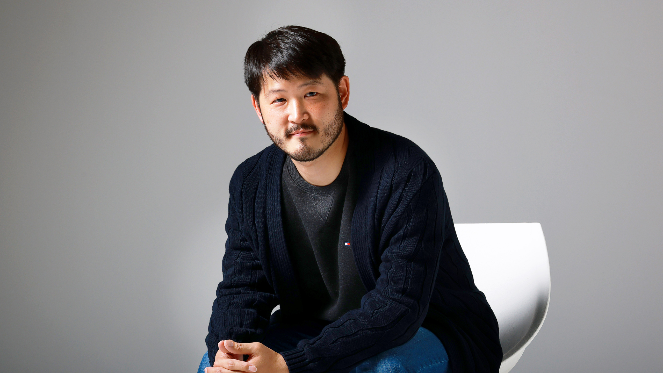Yun Hong Min sitting in a chair leaning forward in front of a gray backdrop