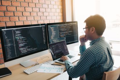 A person sitting at a desk in front of multiple computer monitors and a laptop