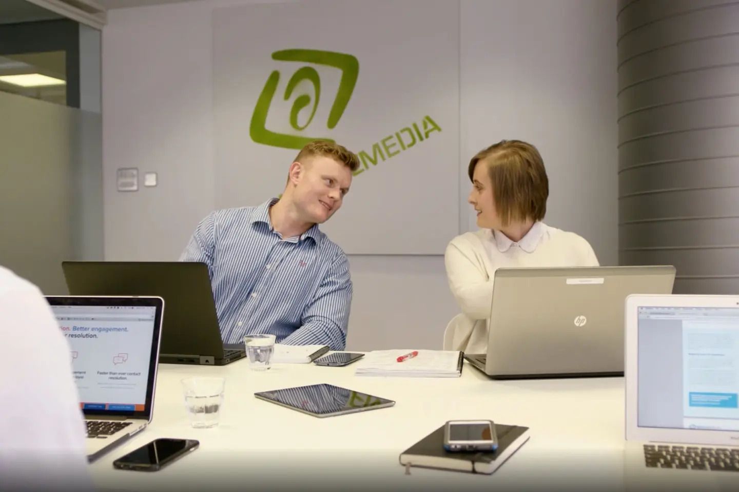 Two people working on laptops at New Voice Media office.