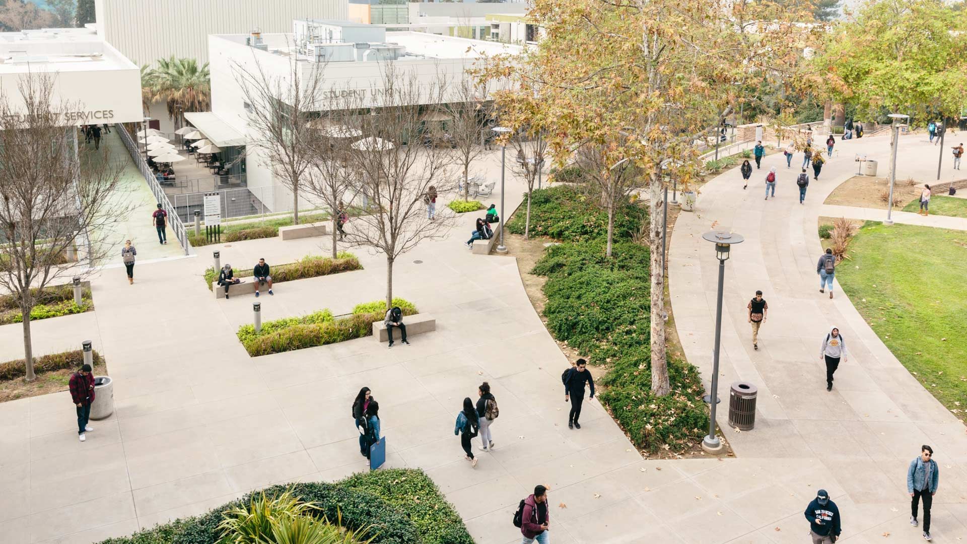 A college campus with green space and walkways populated by students wearing backpacks
