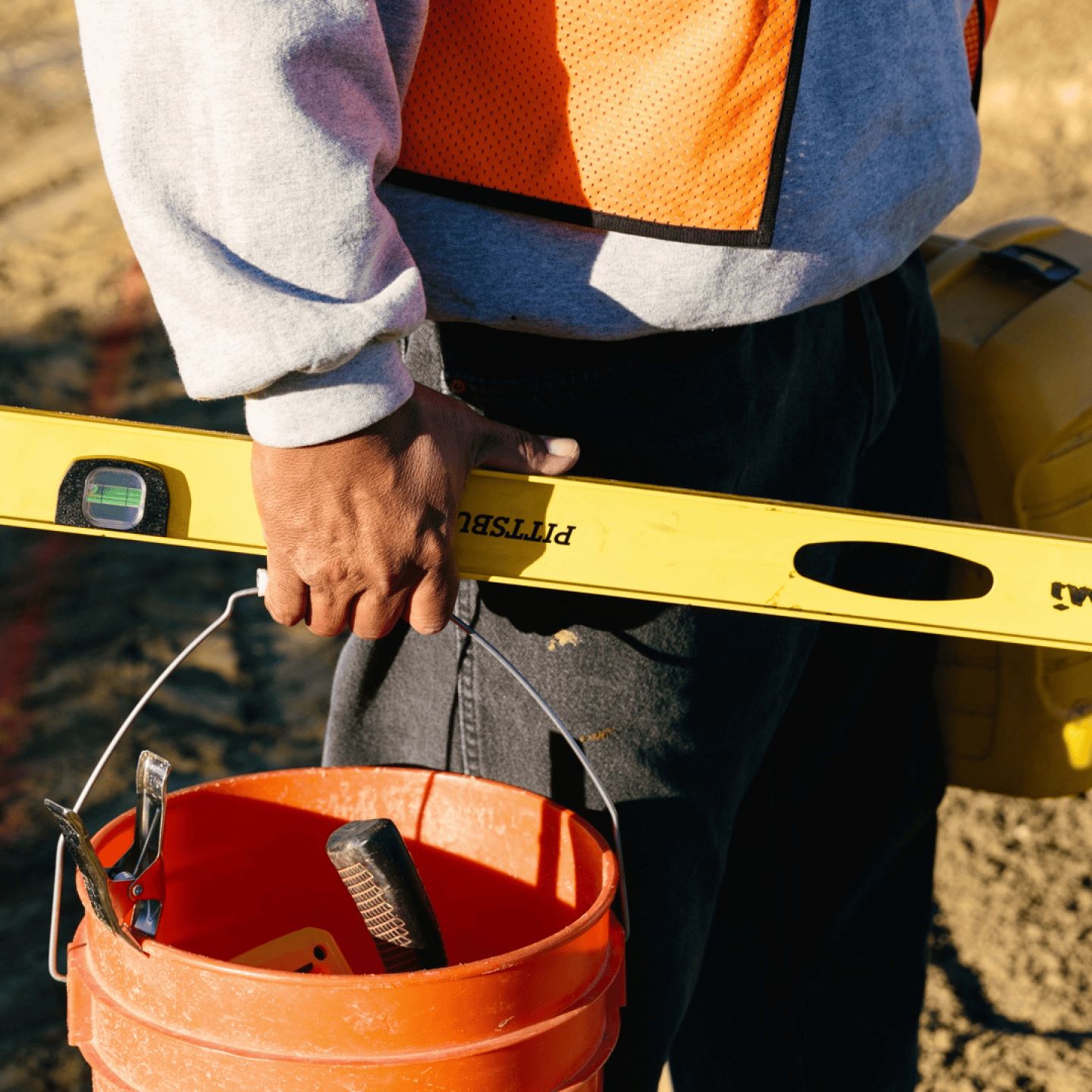Seorang pekerja konstruksi memegang ember dan waterpas
