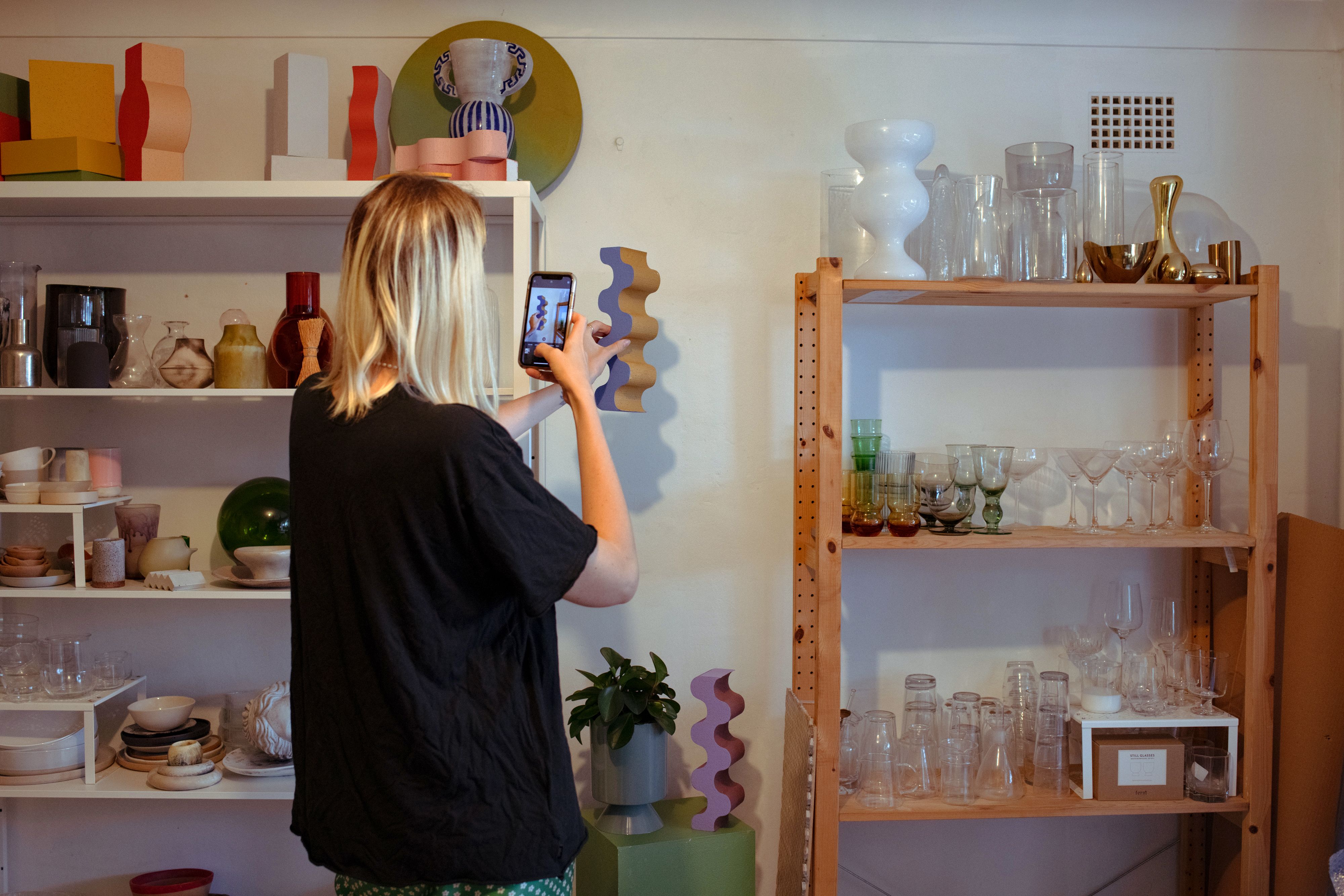 A person uses their mobile device to photograph an ornament from a shelf.