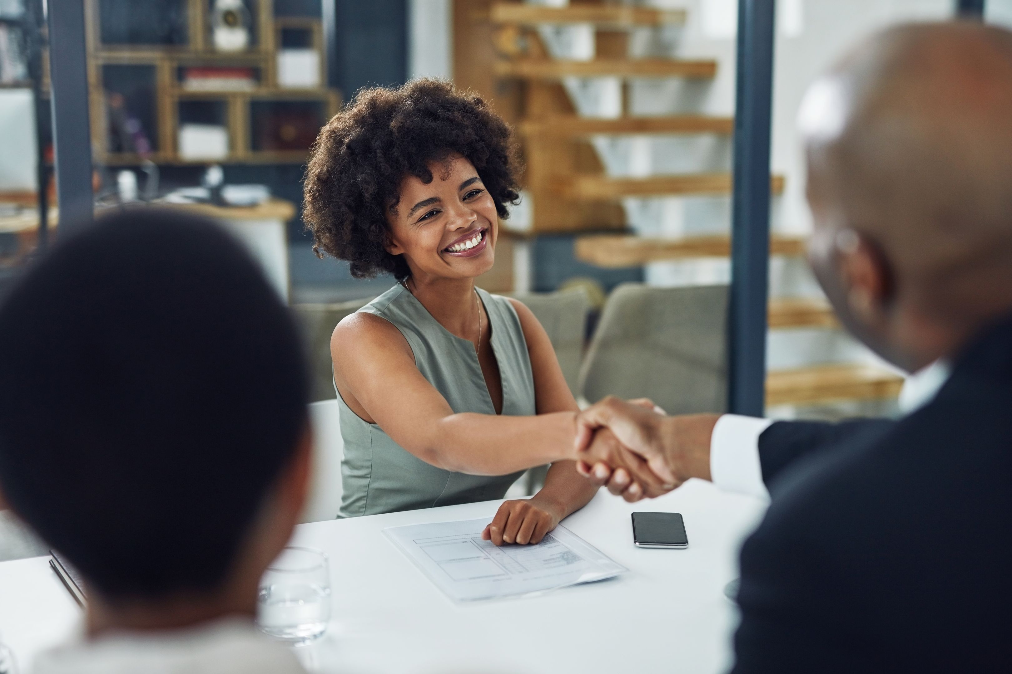 Two people shaking hands across a table in an office.