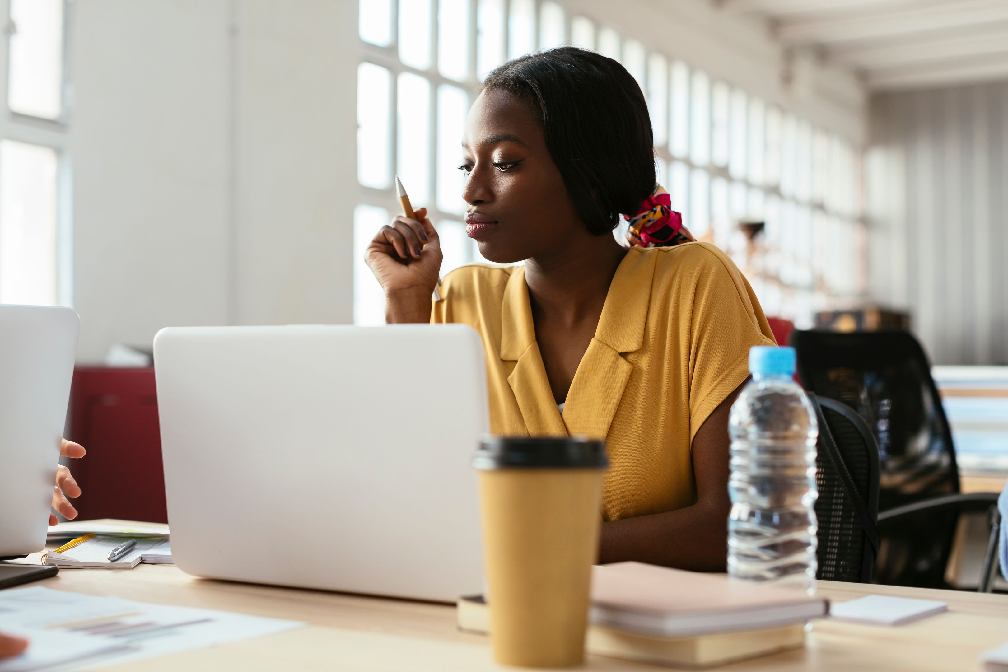A person holding a pen sits at a desk with a laptop.