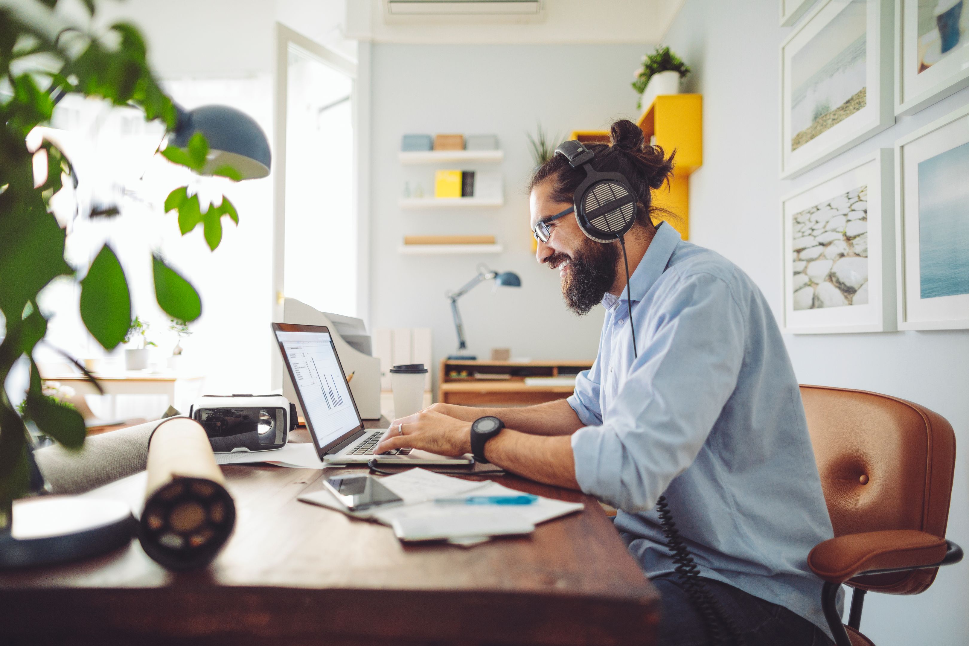 A person wearing headphones in their home office smiles at their laptop.