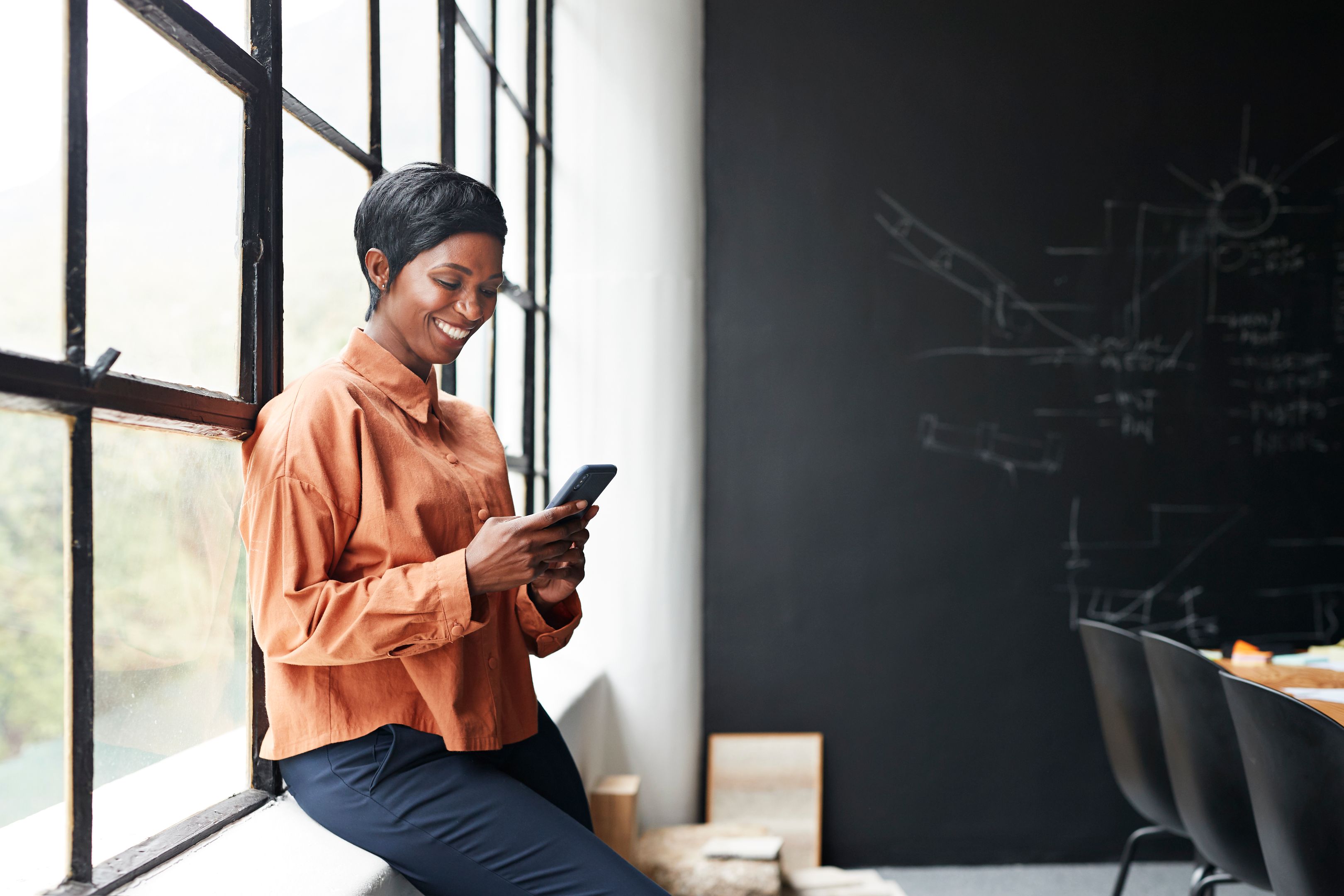A person on their mobile device sitting on a window ledge in an office.