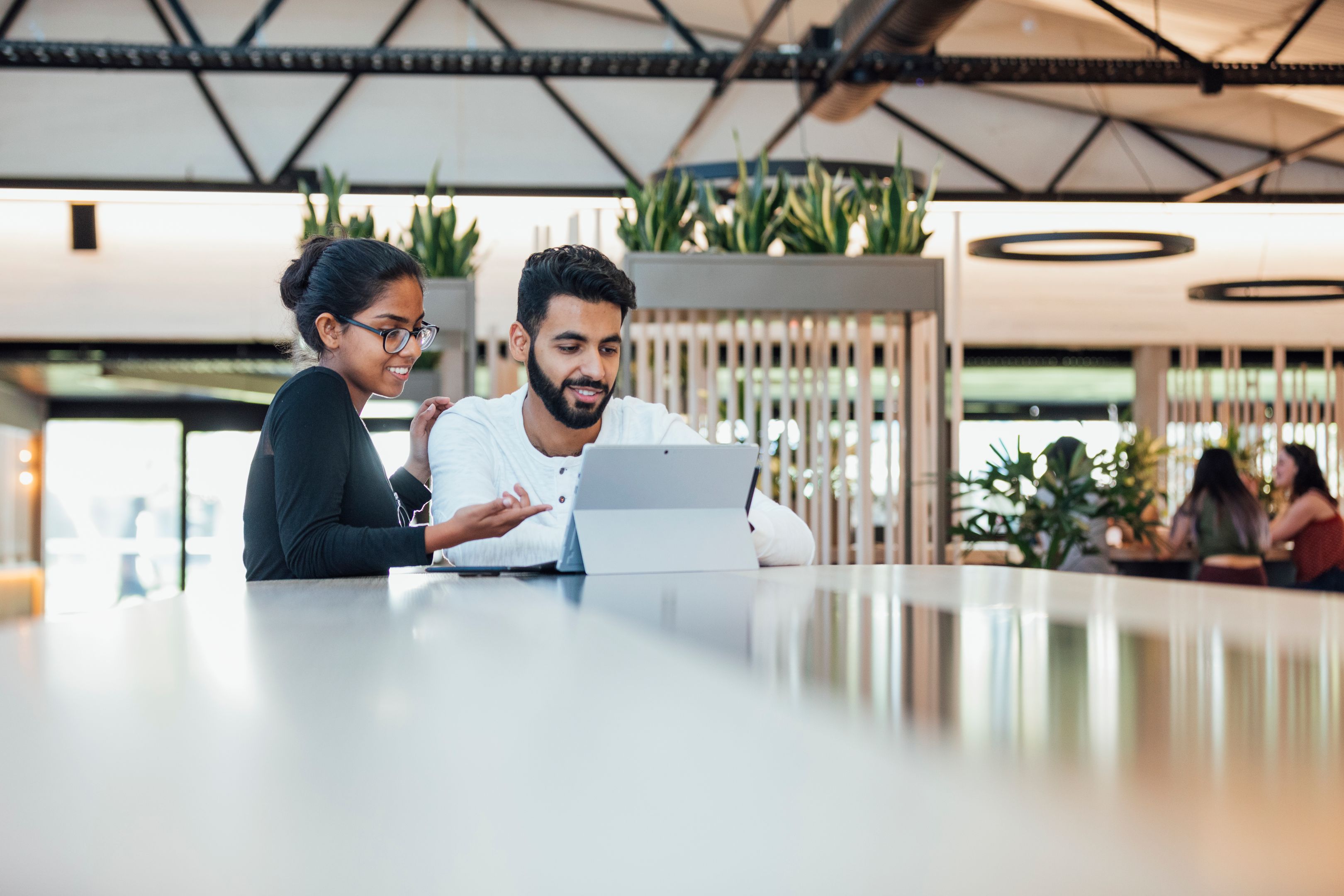 Two workers stand close together looking over a laptop as the female worker supports her male colleague.
