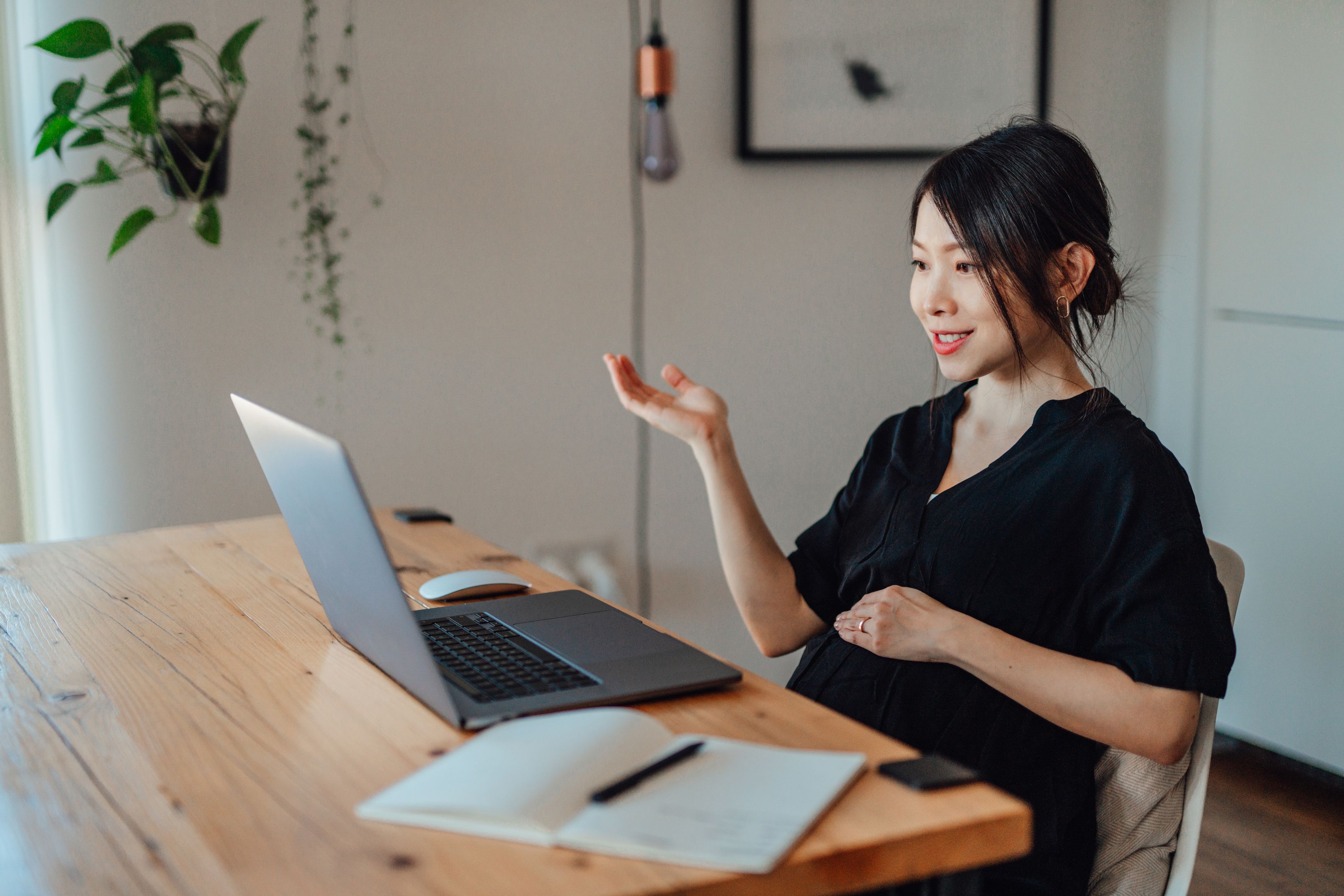 A person sits at their desk during a virtual meeting while looking at a notepad and smiling.