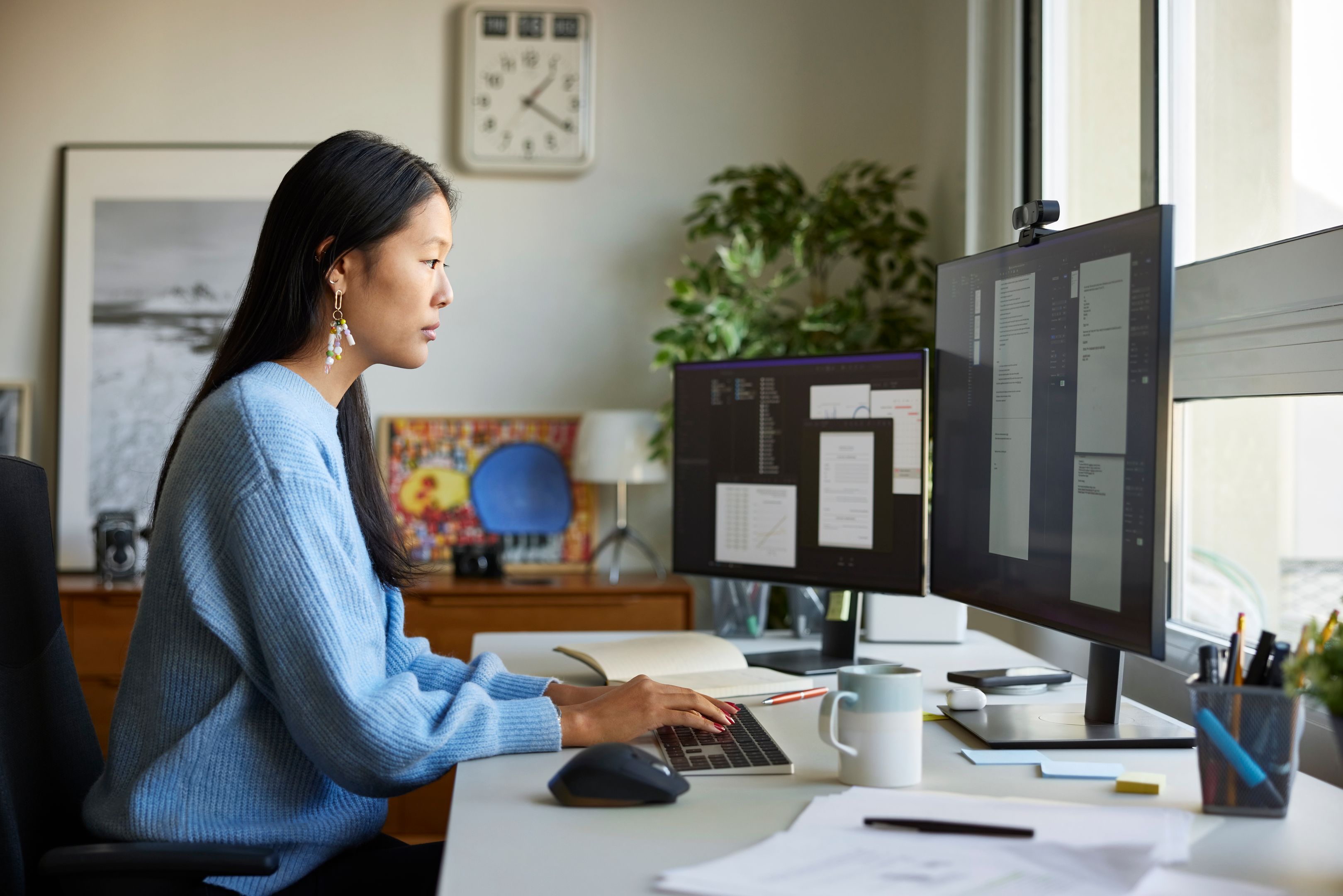 A person works from two monitors in a home office.