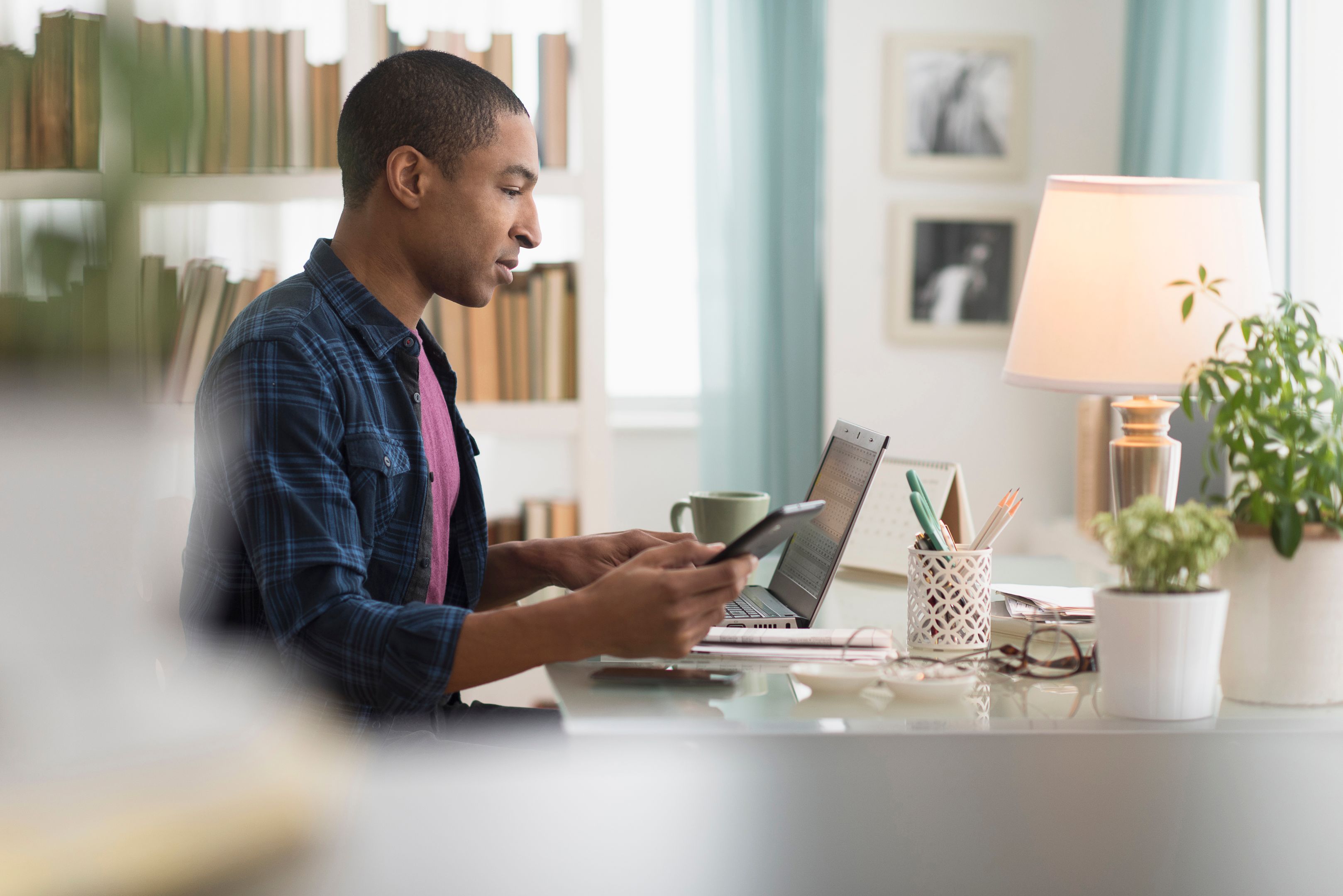 A person holds their mobile device while working from a laptop at home.